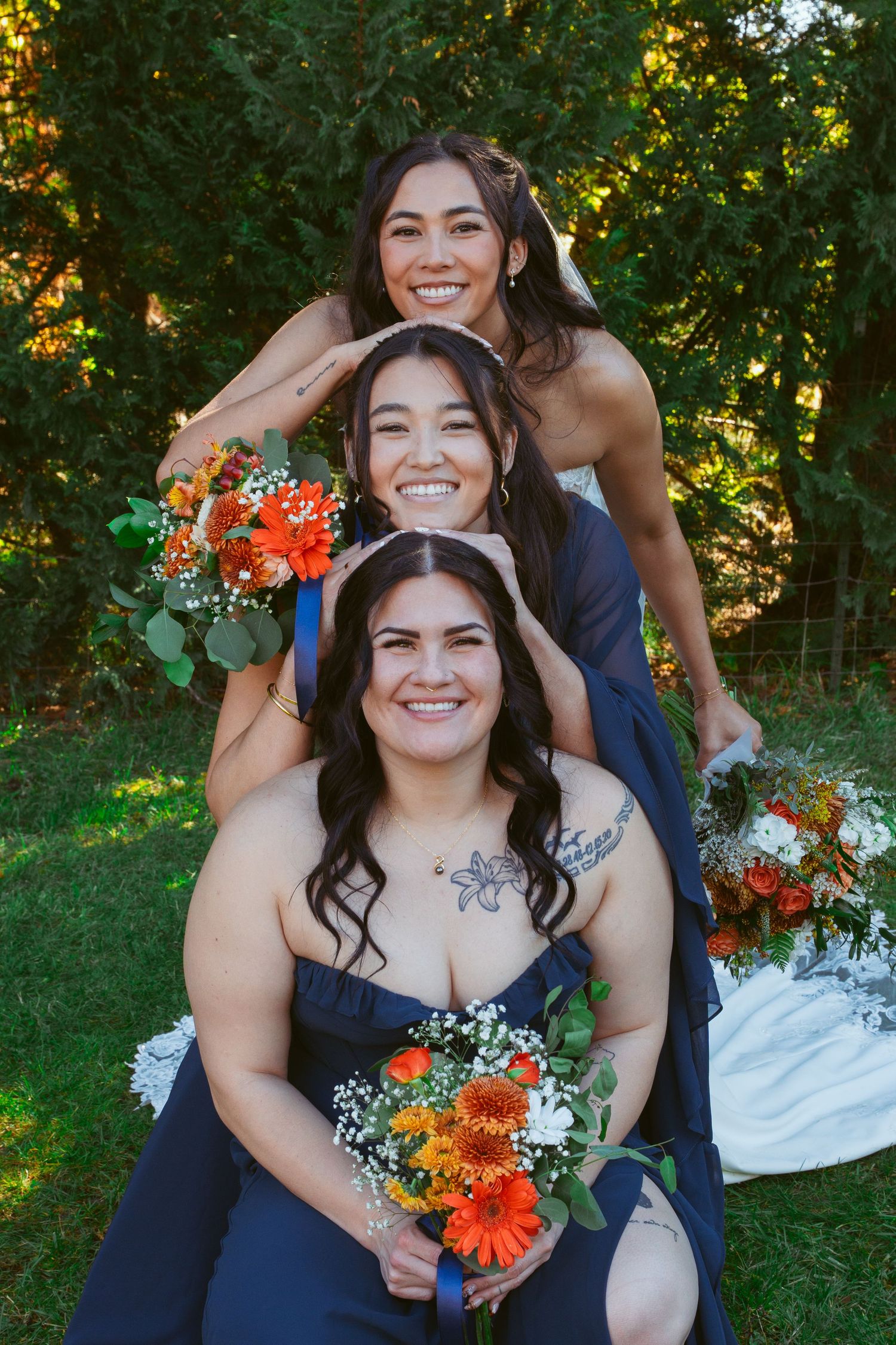 Three people stacked in playful pyramid pose with orange bouquets during wedding photoshoot.