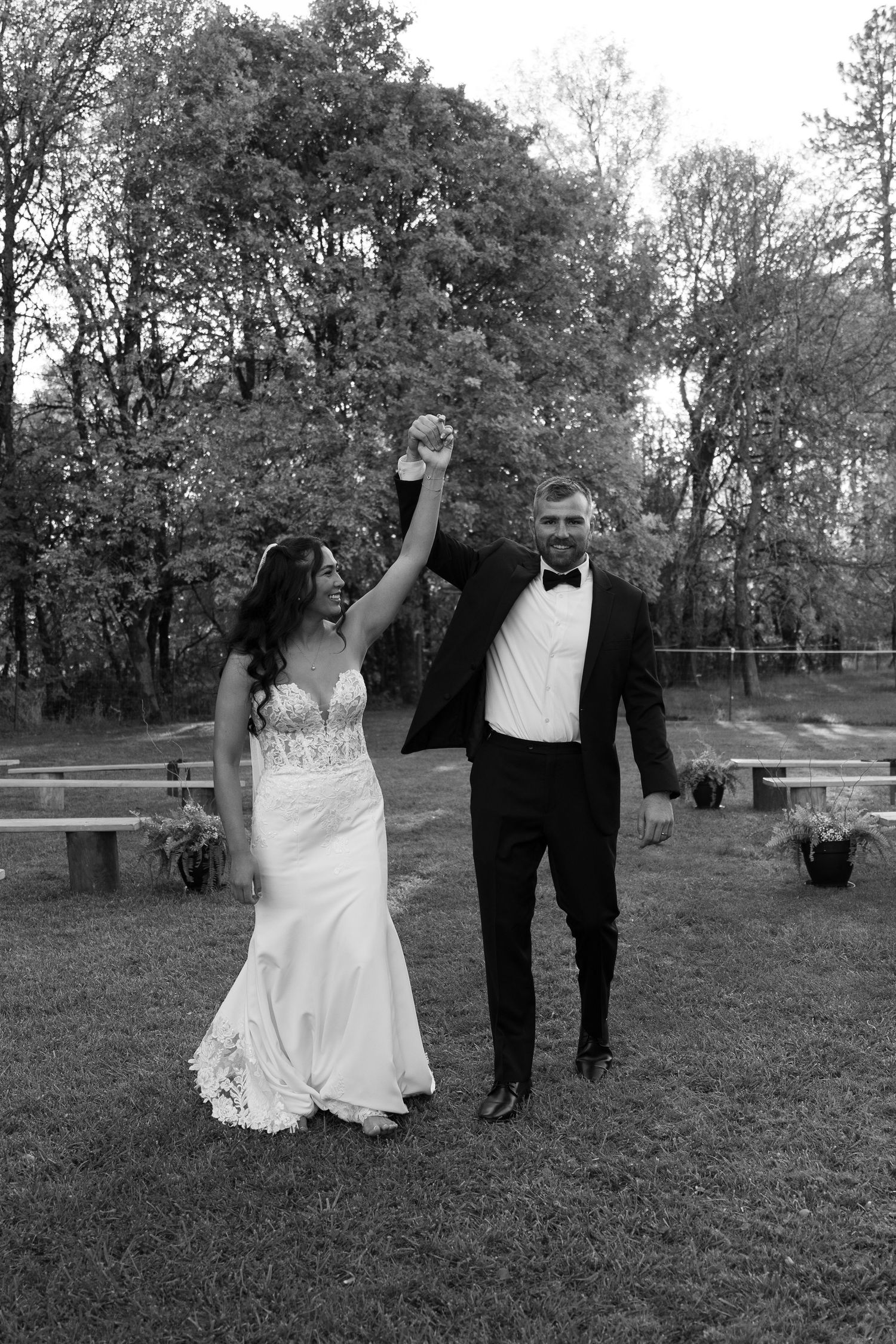 Celebratory black and white photo of newlyweds raising joined hands in victory pose.