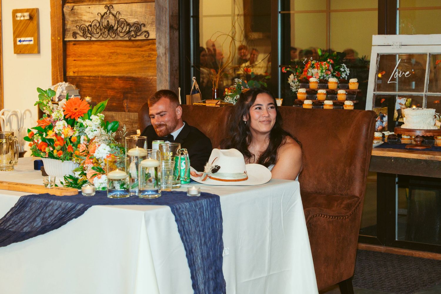 Wedding reception tables decorated with floral centerpieces and white linens in an indoor venue.