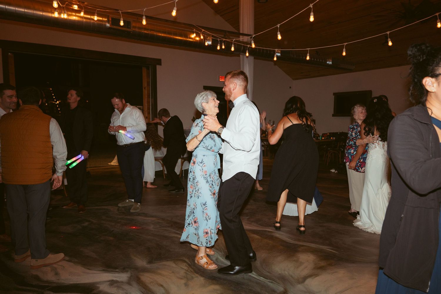 Couples dancing together at an indoor wedding reception with string light ambiance.