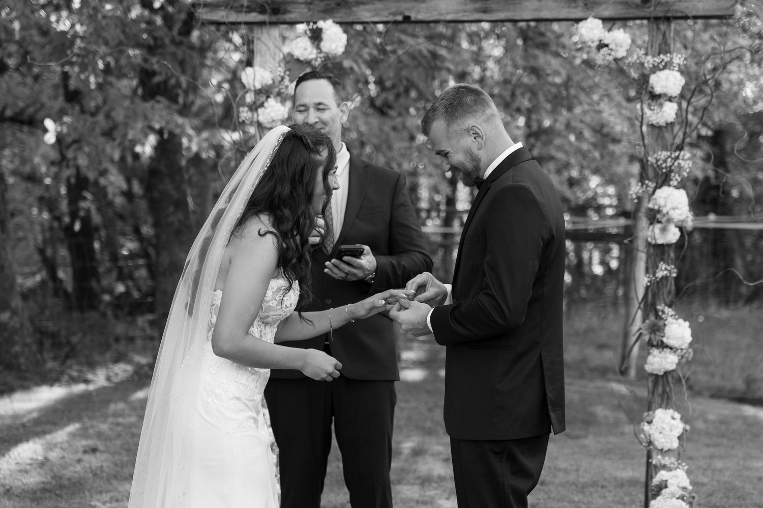 Black and white photo of wedding ceremony under floral-decorated arch.