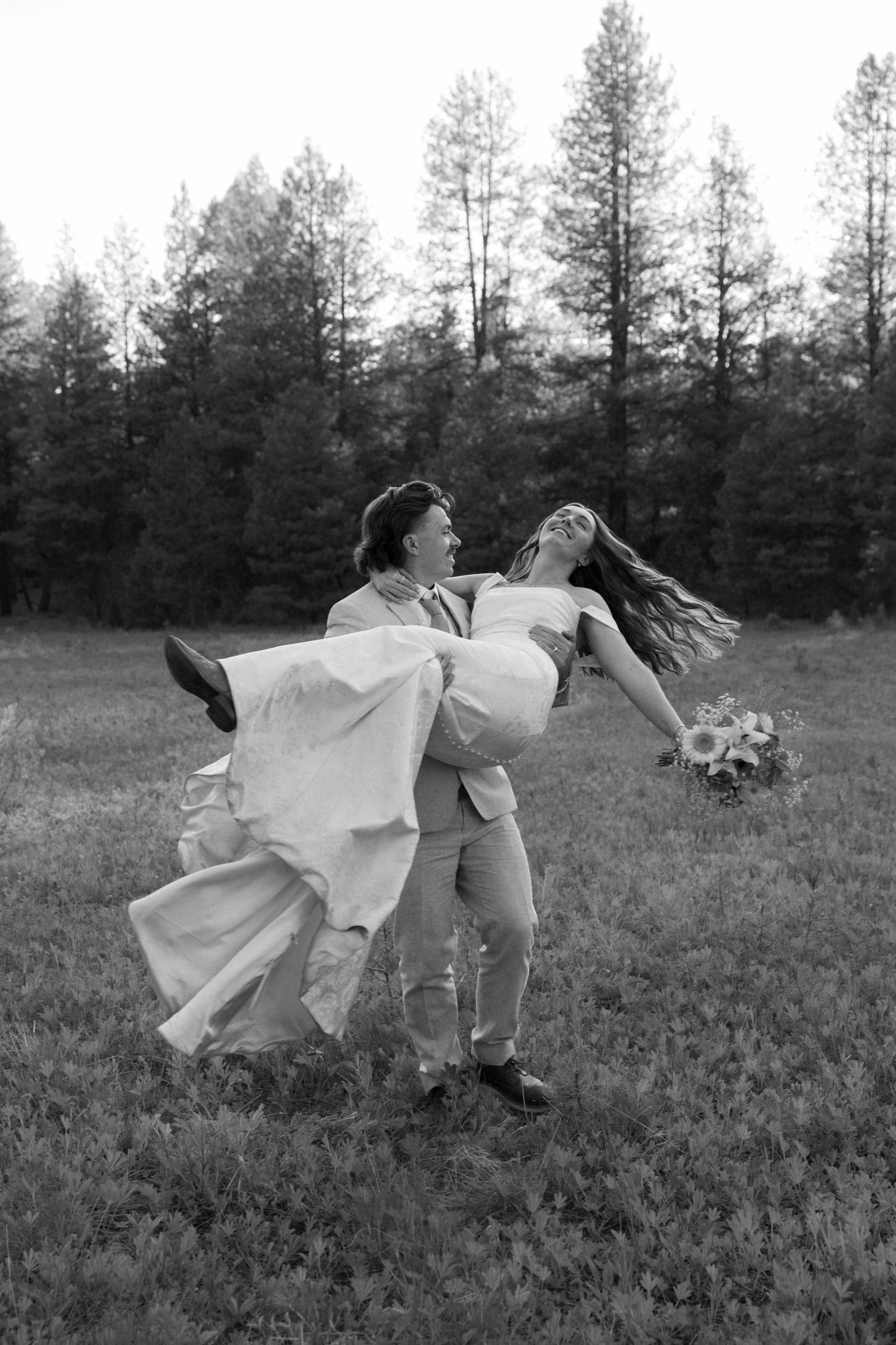 A black and white capture of a couple performing a dramatic dance dip in a grassy field.