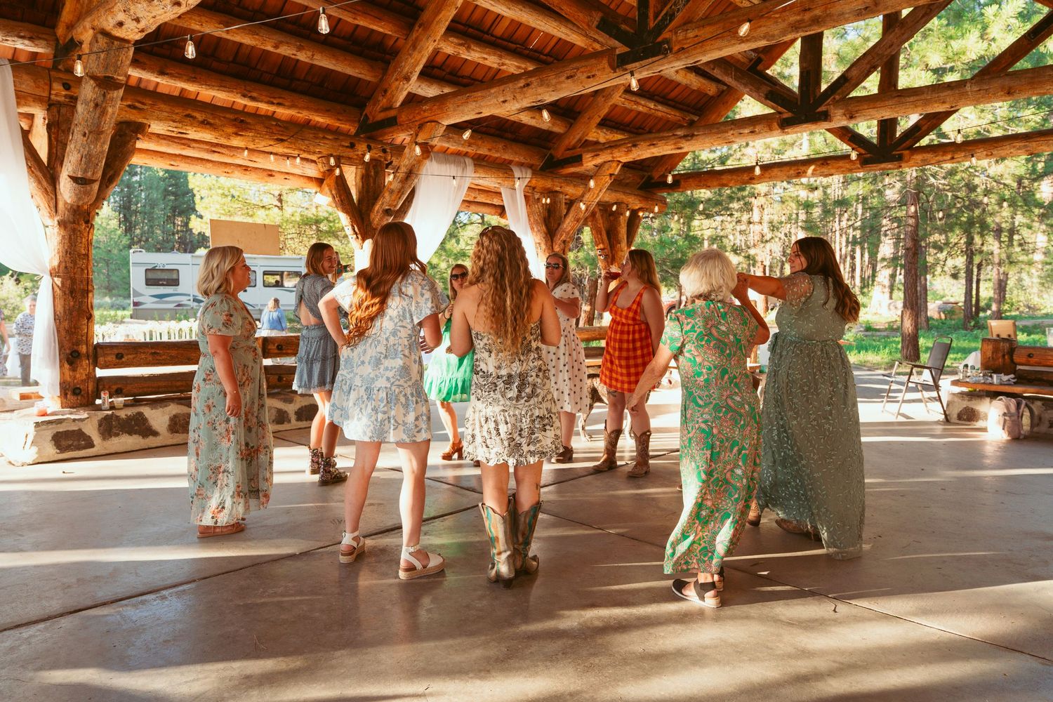 Guests dancing and celebrating under a wooden pavilion with natural forest backdrop.