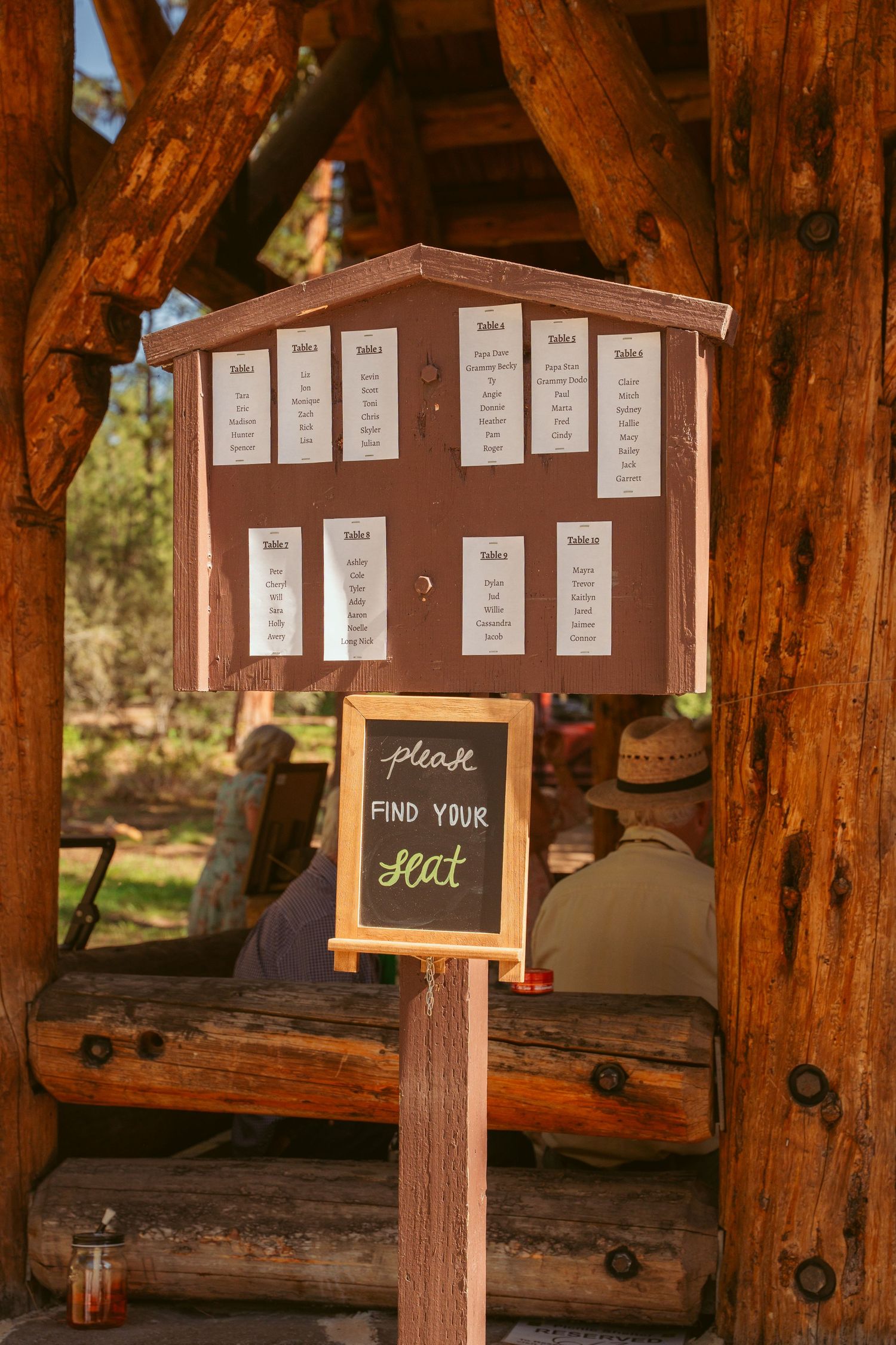 Brown wooden seating chart displays with name cards arranged under a rustic pavilion.