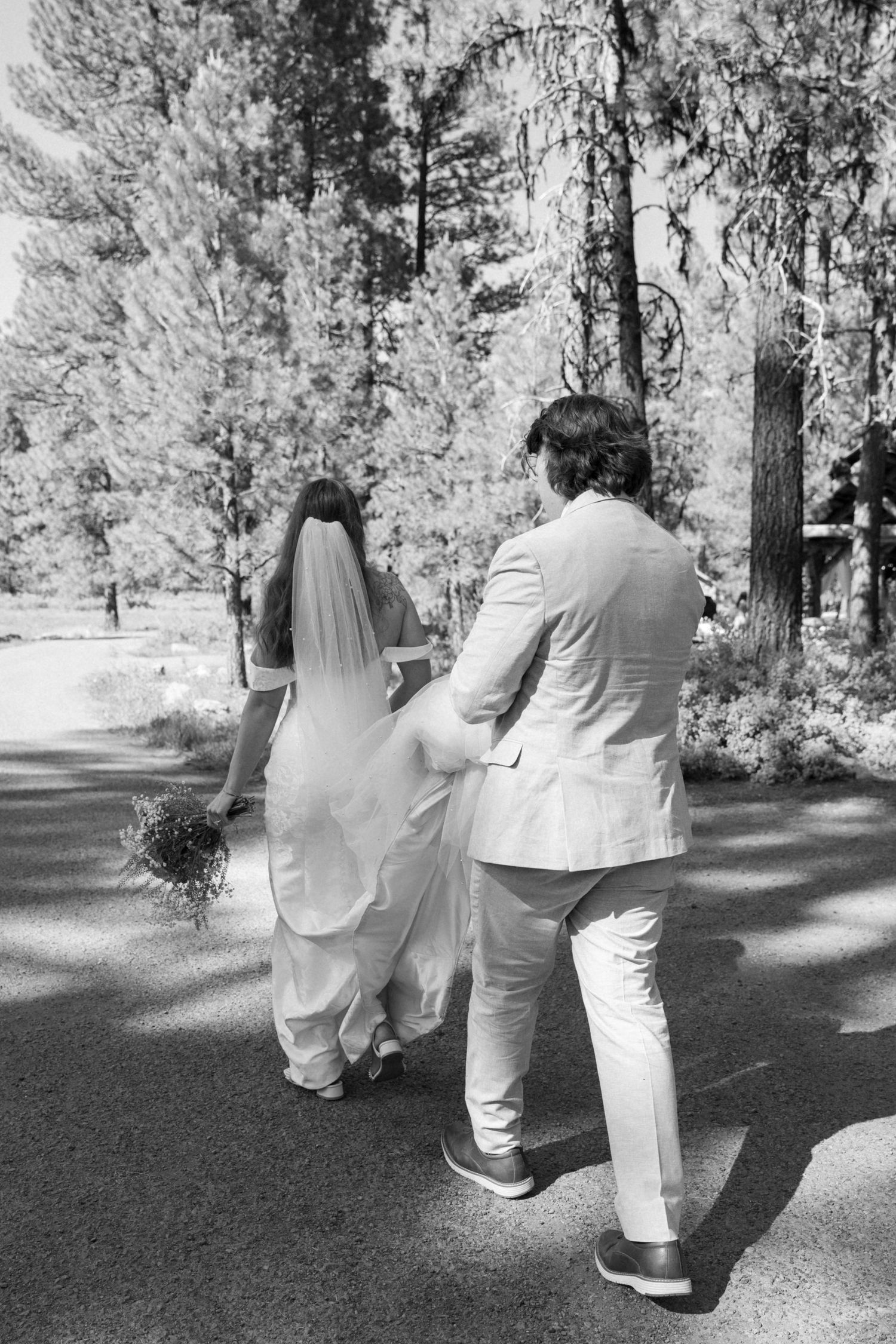 A black and white capture of a couple walking down a forest path during their wedding day.