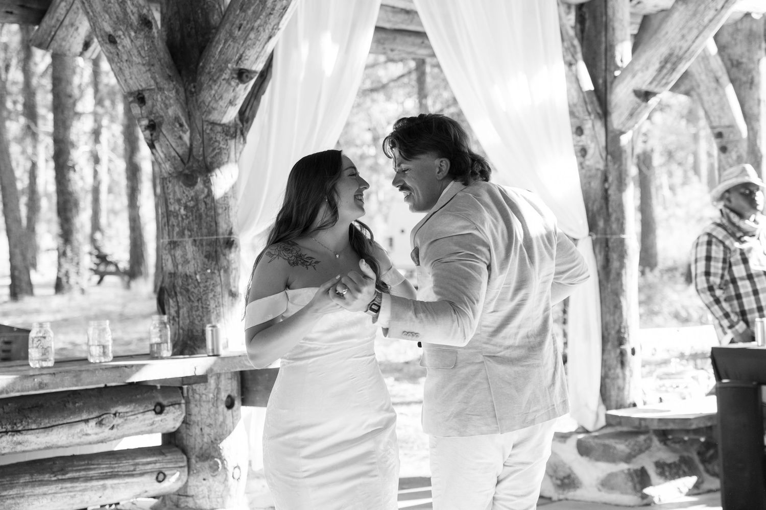 Black and white photo of a dance sequence in an outdoor wedding venue with forest backdrop.