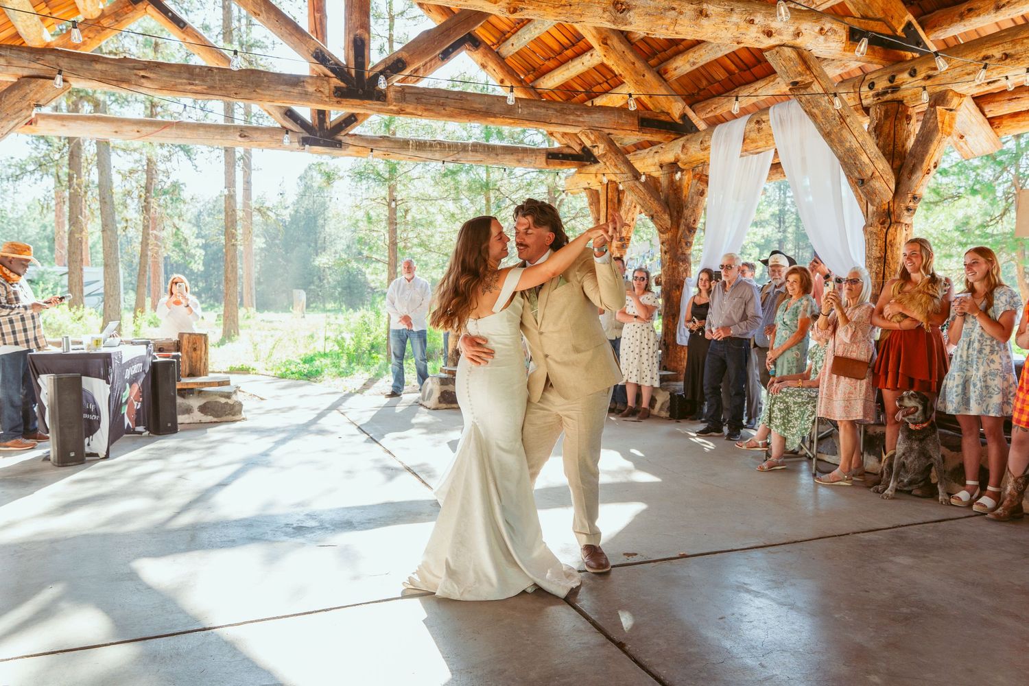 Wedding couple performs romantic dance moves in a timber-frame venue with onlooking guests.