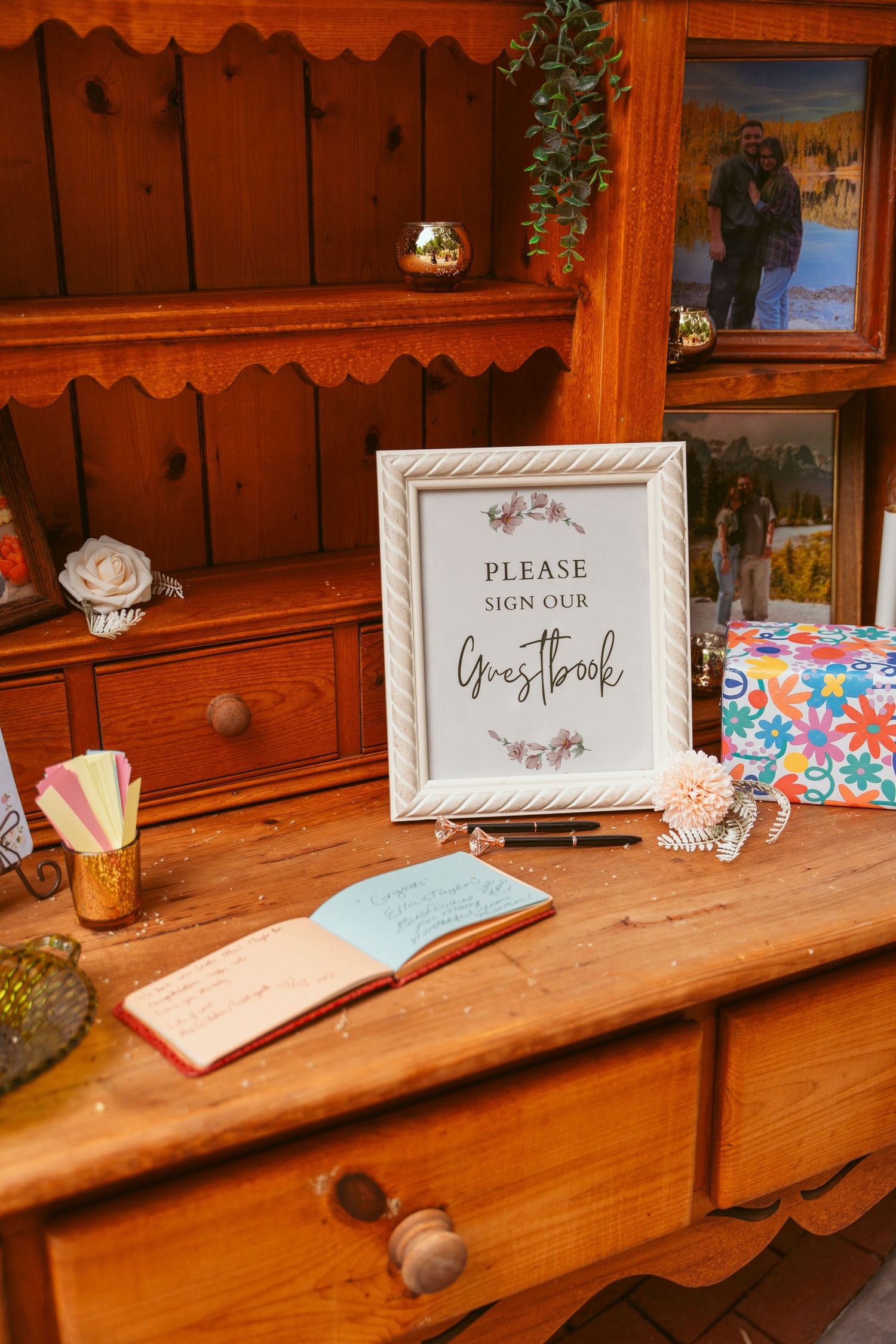 Wooden shelf displaying wedding signage and guest books with rustic decor.