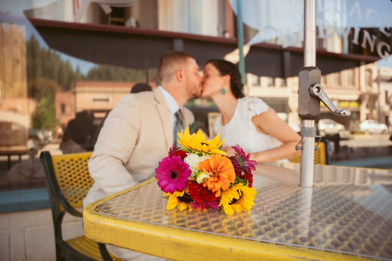 Newlyweds enjoying intimate moment at cafe table decorated with bright sunflowers.