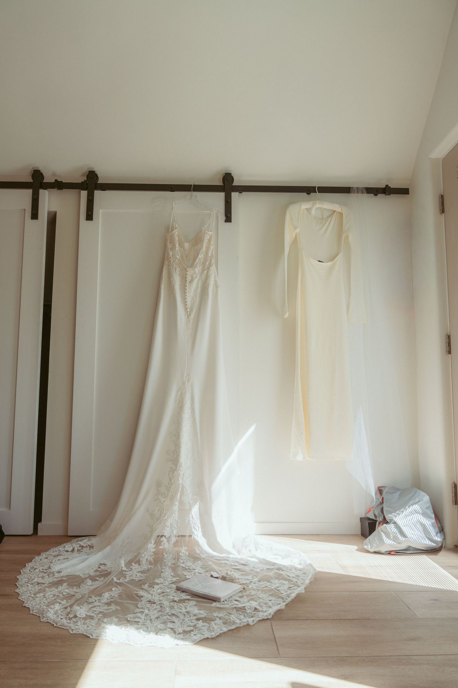 Wedding gowns with lace details displayed on hangers against a minimalist white wall.