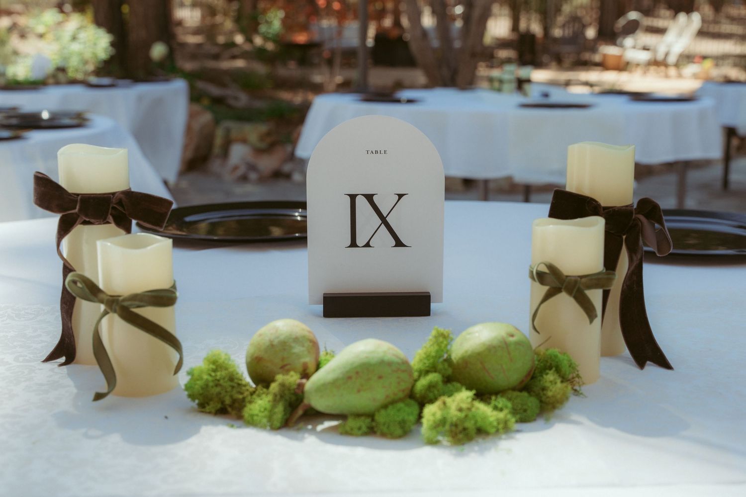 White candles and greenery decorate elegant table settings at an outdoor wedding reception.