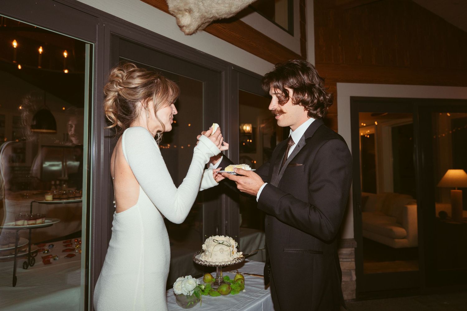 Couple shares playful moment during wedding cake tradition at evening reception.