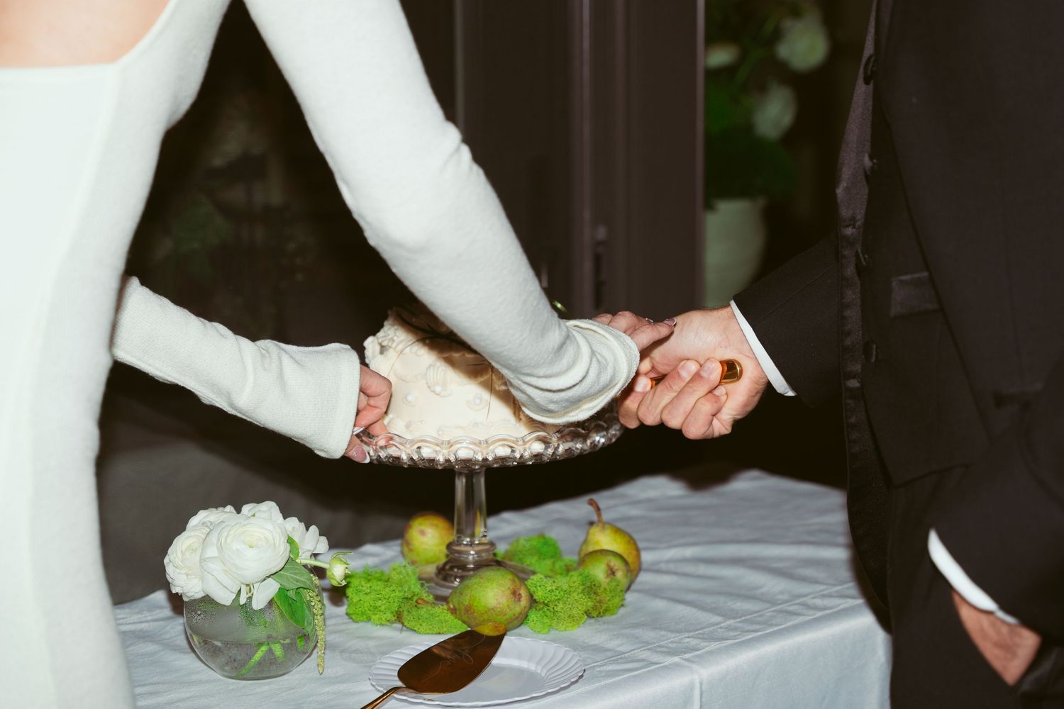 Wedding couple serves cake at their reception with white tablecloth and decorative settings.