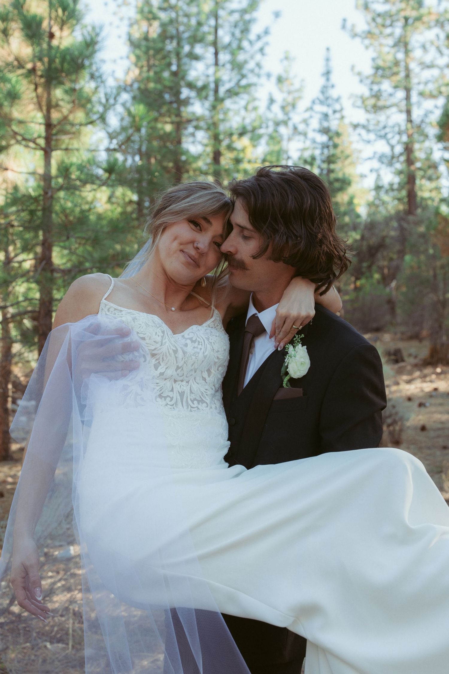 A tender moment between newlyweds as the bride's white dress flows in the forest setting.
