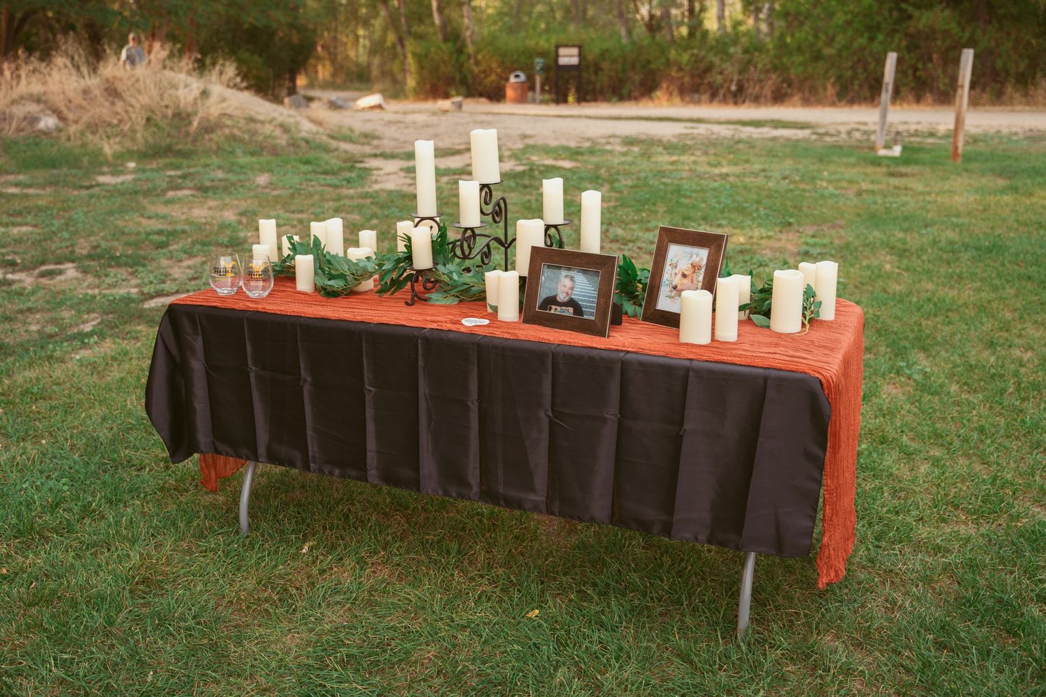 Long tables with black chairs set up outdoors for a wedding reception with white candle centerpieces.