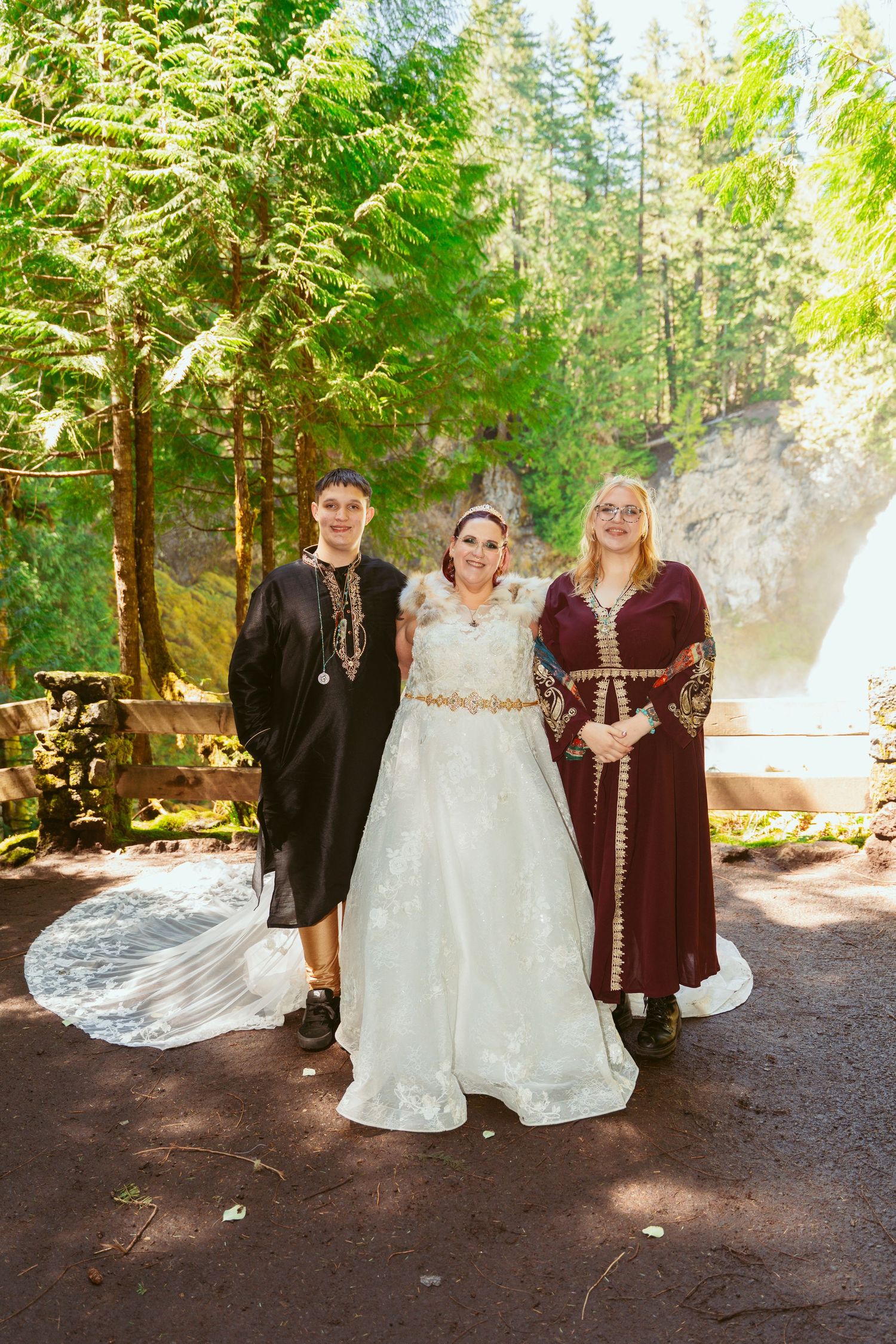 A wedding group in medieval costumes poses for formal photos in a forest clearing.