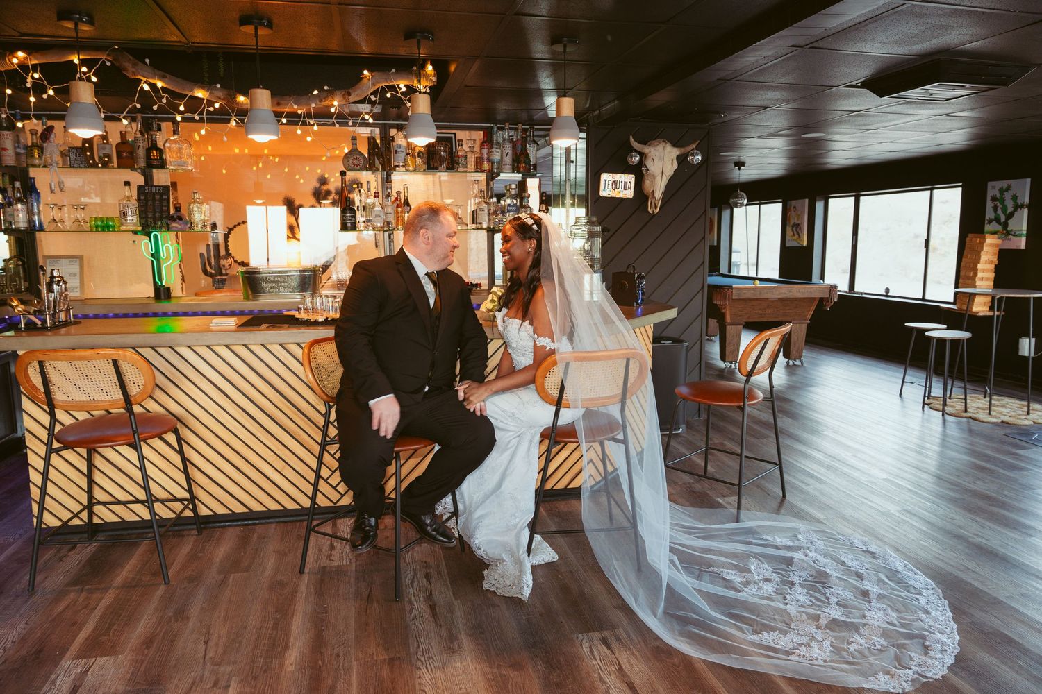 Newlyweds share an intimate moment at a bar with dramatic lighting and decor.