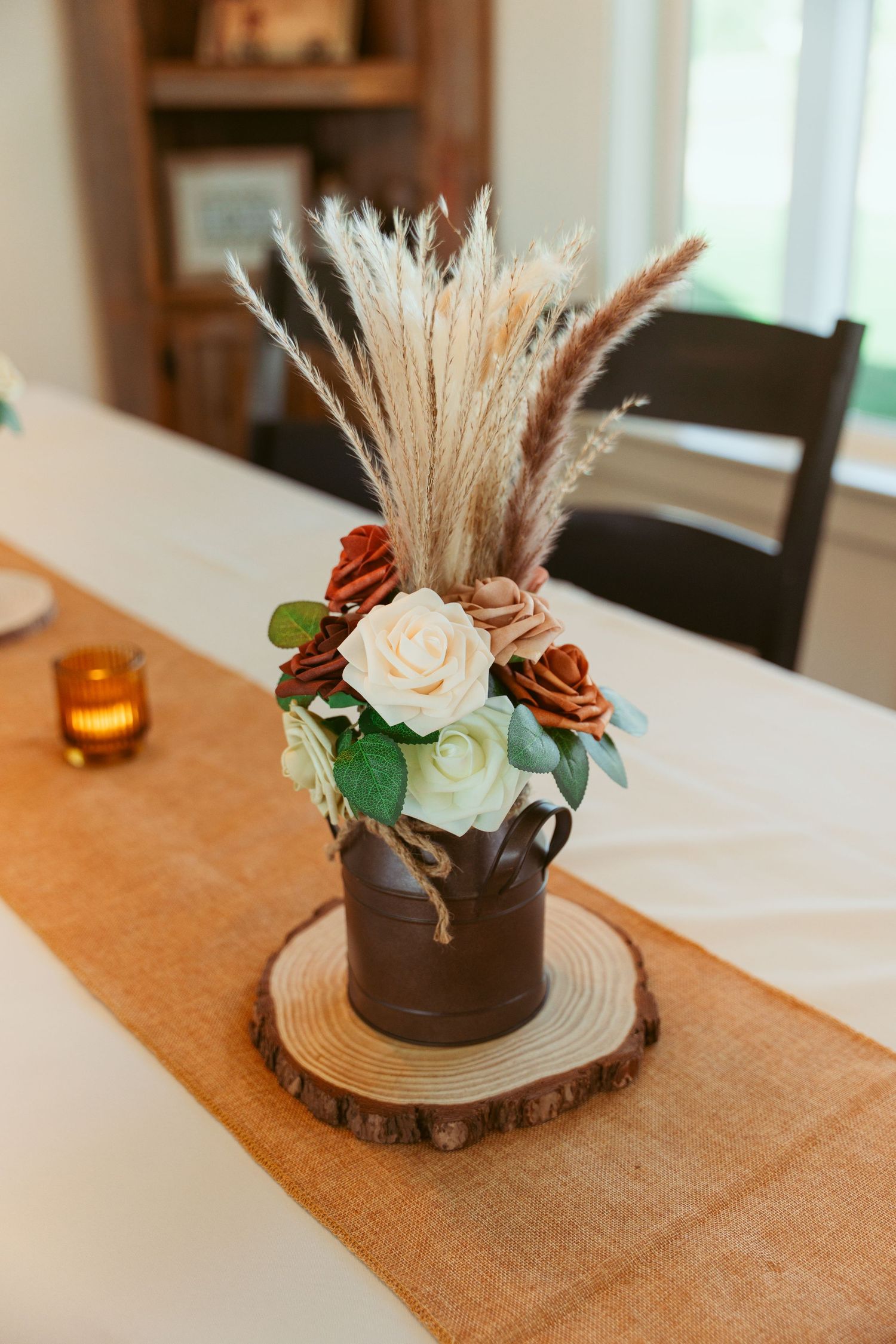 Rustic floral centerpiece with dried pampas grass and roses on a wooden slice base.