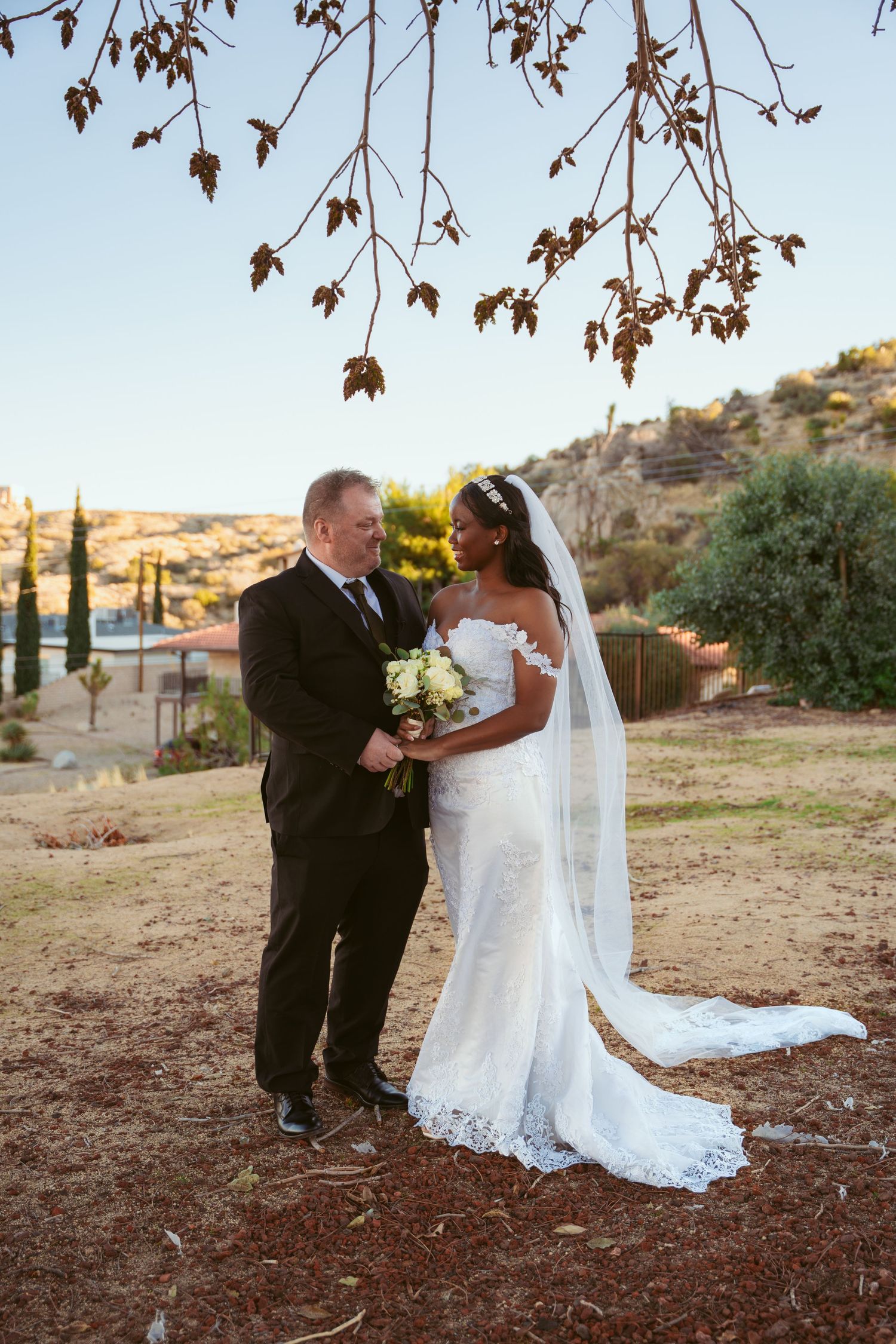 A couple in wedding attire poses under autumn leaves in a desert setting.