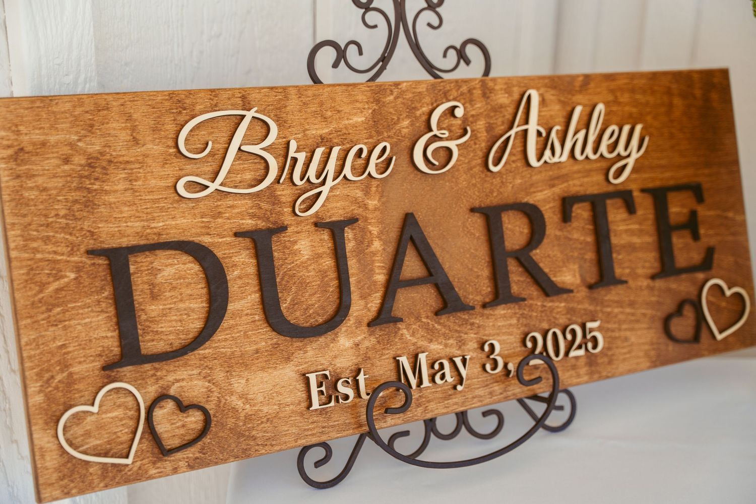 Rustic wooden signs with cursive text and decorative hearts displaying names and dates.
