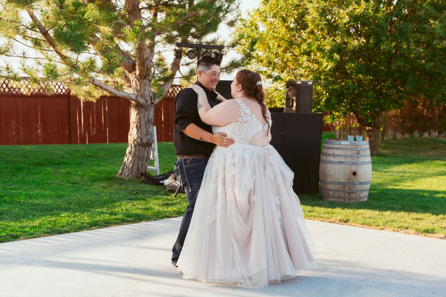 Couple dancing together on an outdoor patio with trees and a red barn in the background.