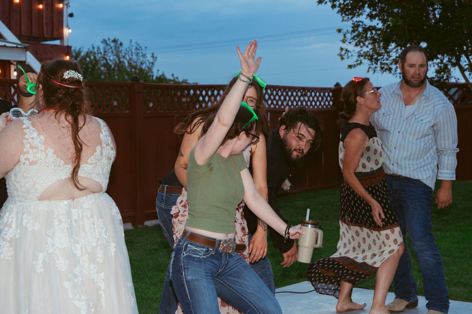 People dancing energetically at an outdoor party with string lights visible in the background.