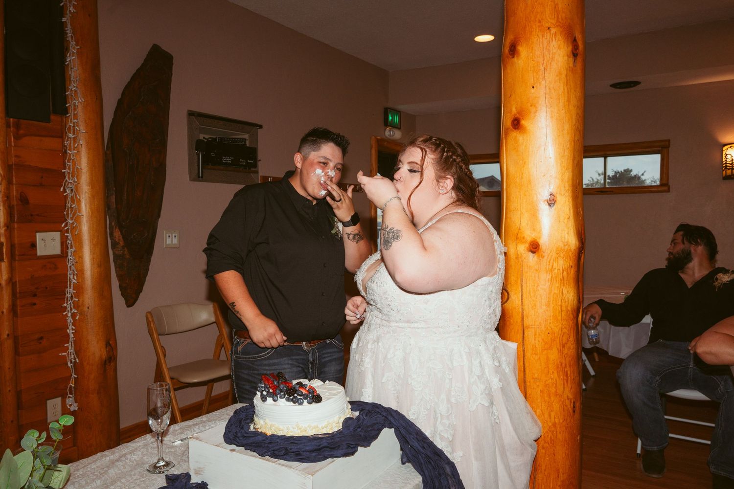 A couple playfully smashes wedding cake into each other's faces during their reception celebration.