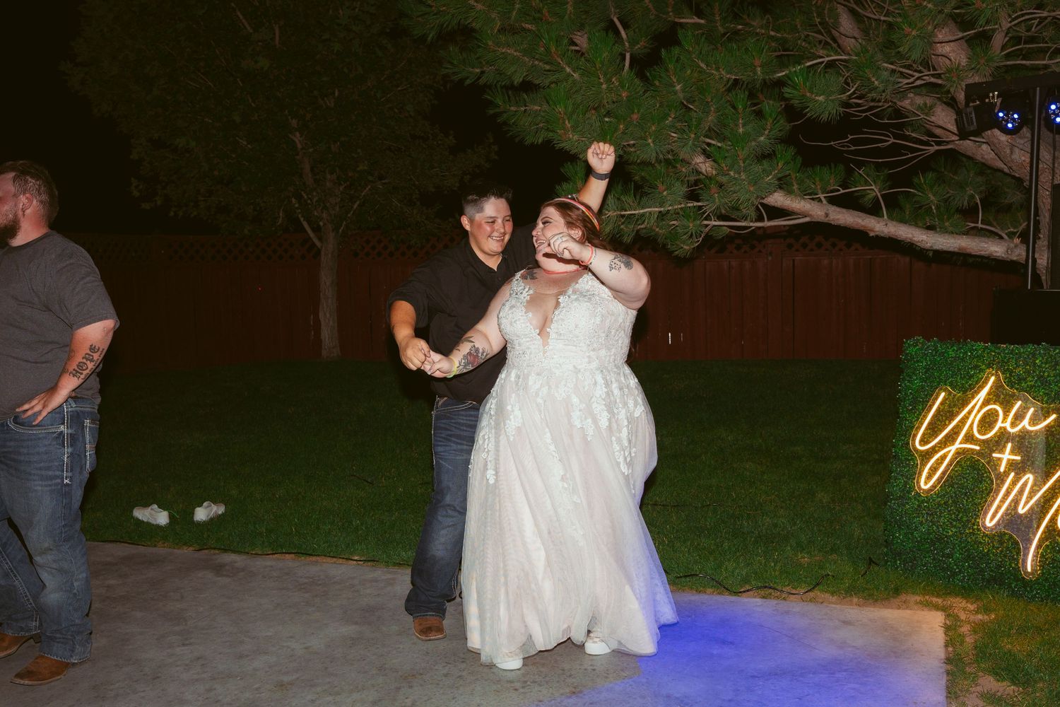 People dancing on an outdoor patio with illuminated neon signage in the background.