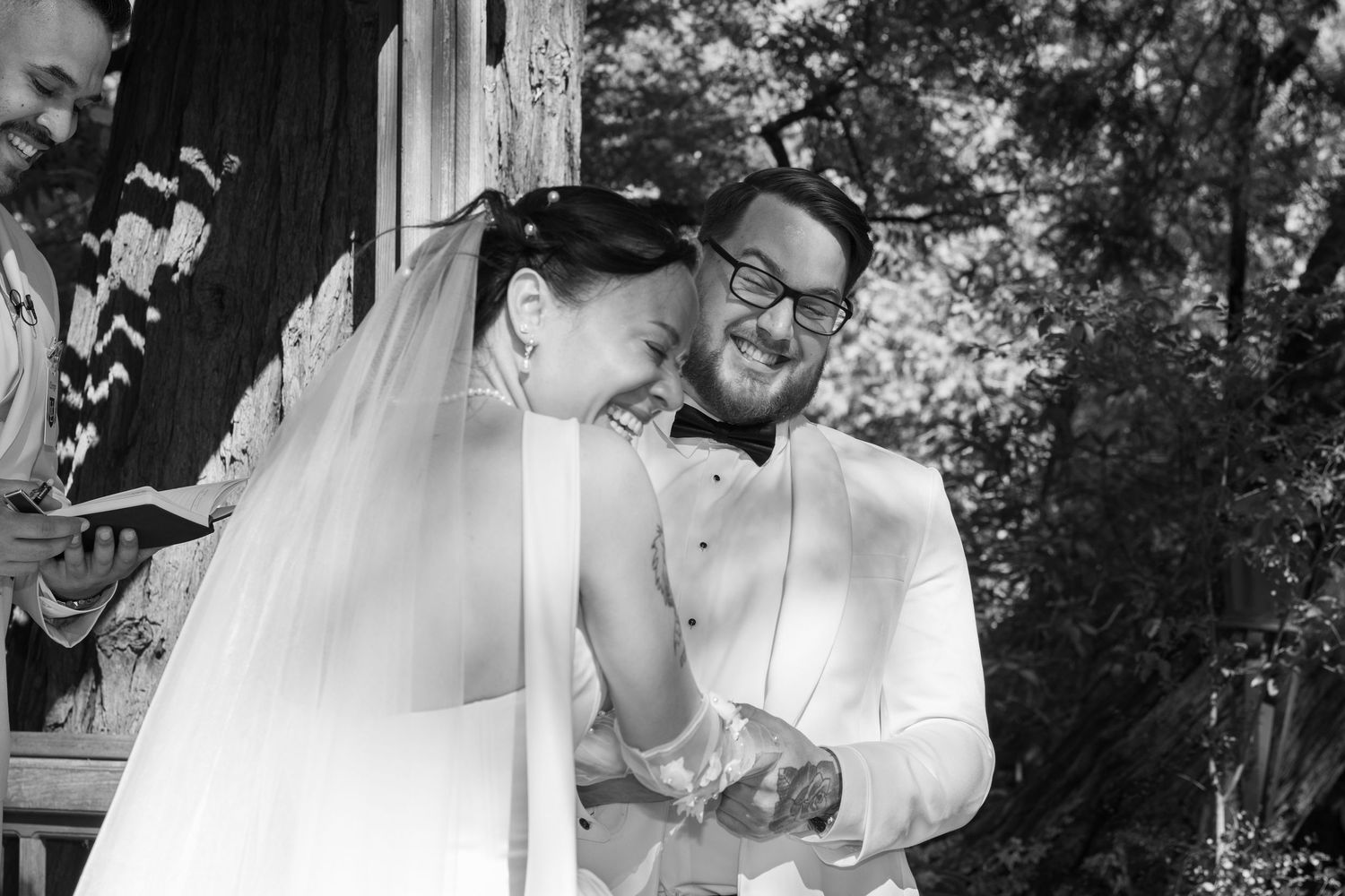 Black and white candid moment during wedding ceremony under wooden gazebo.