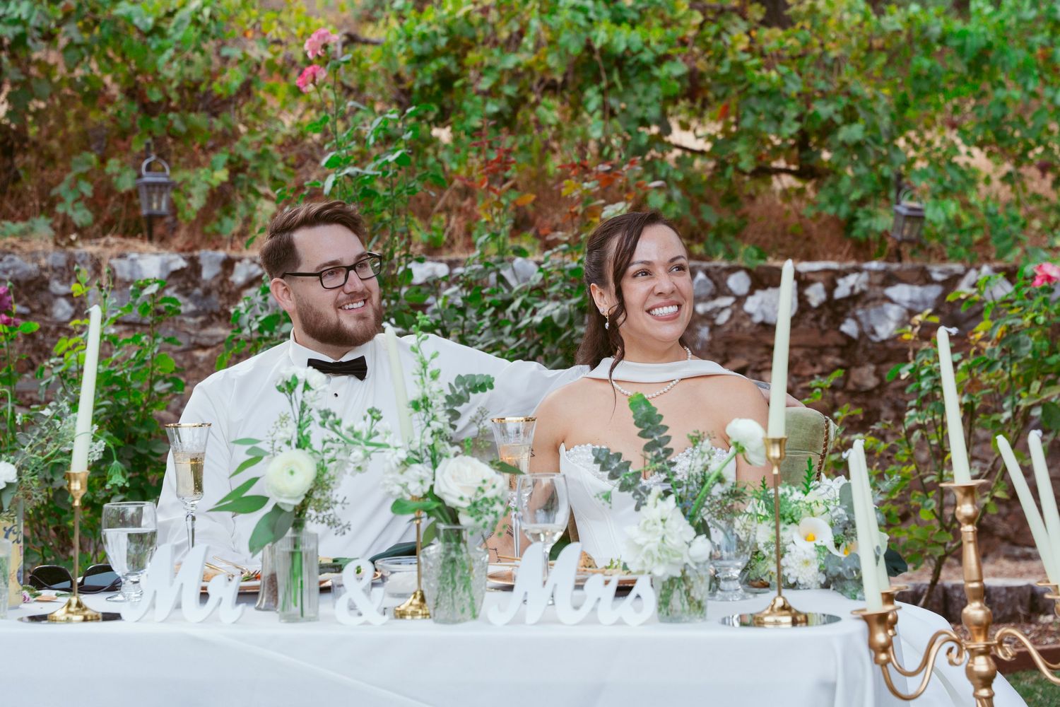 Wedding guests seated at decorated outdoor tables under trees with string lights overhead.