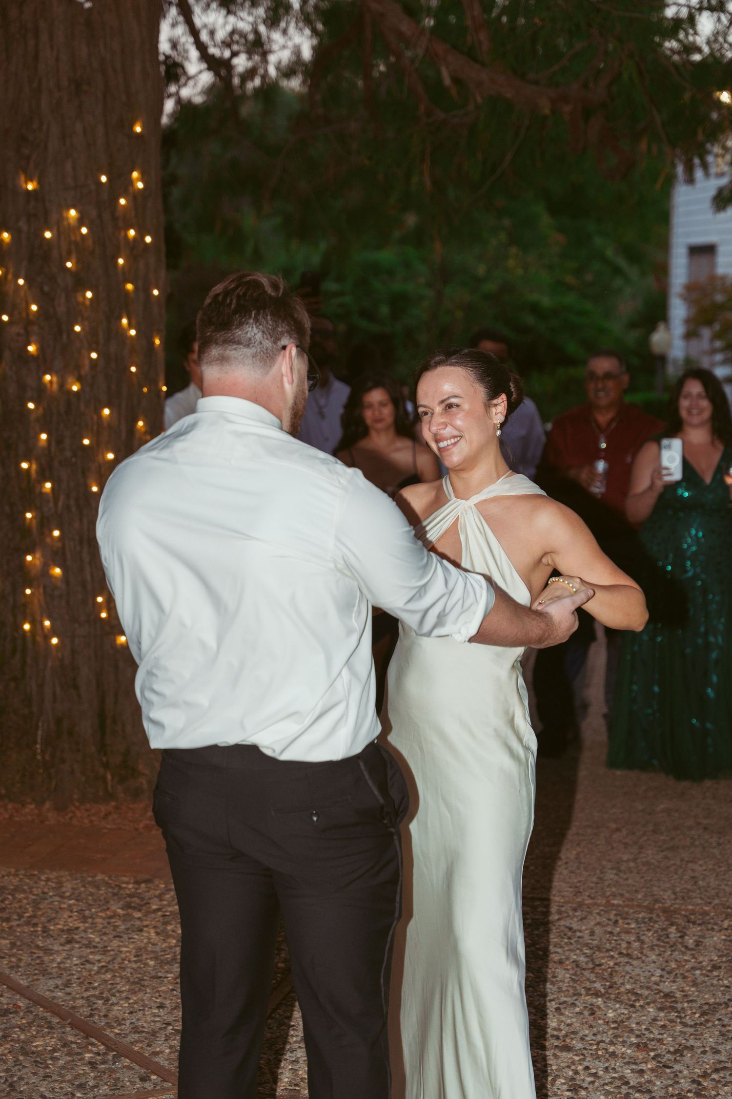 Couples twirl and dance on a rustic outdoor dance floor illuminated by string lights.