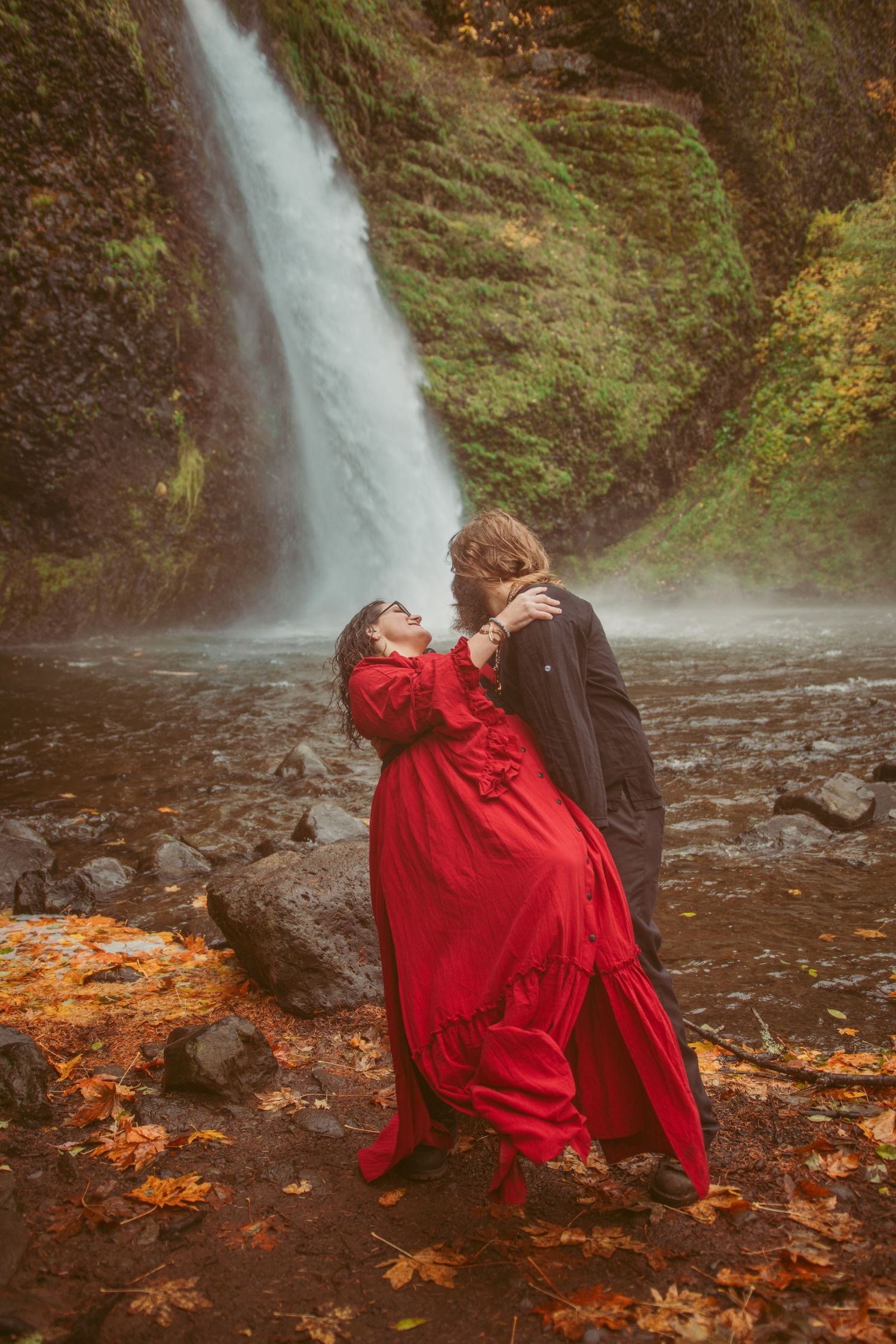 Dancing couple in red and black creates romantic moment by waterfall.