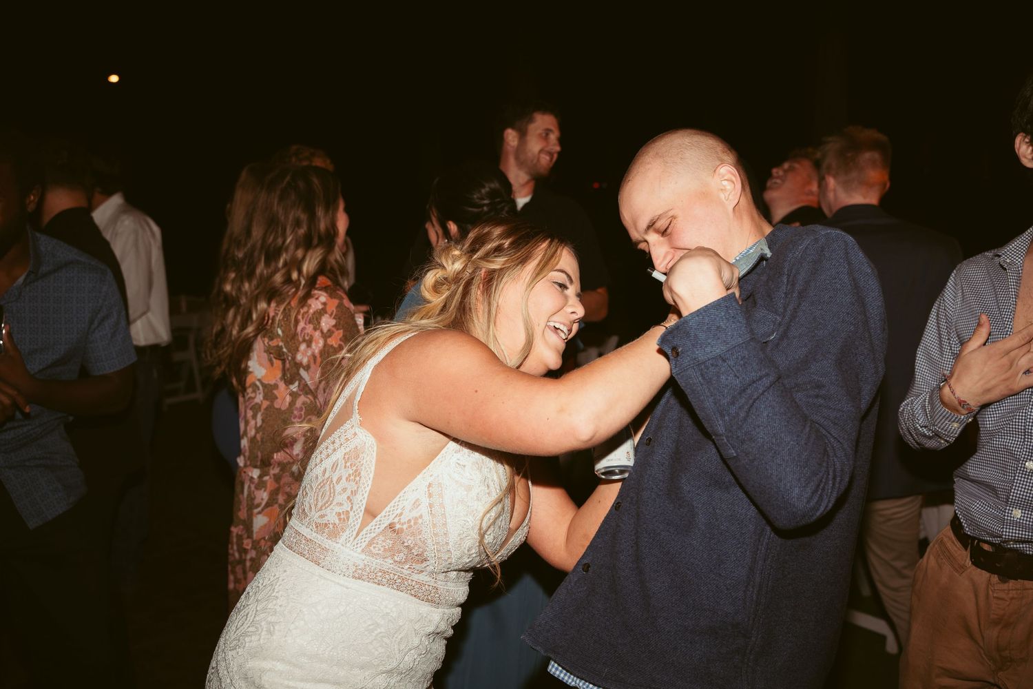 Wedding guests dancing and celebrating on a dimly lit dance floor with string lights overhead.