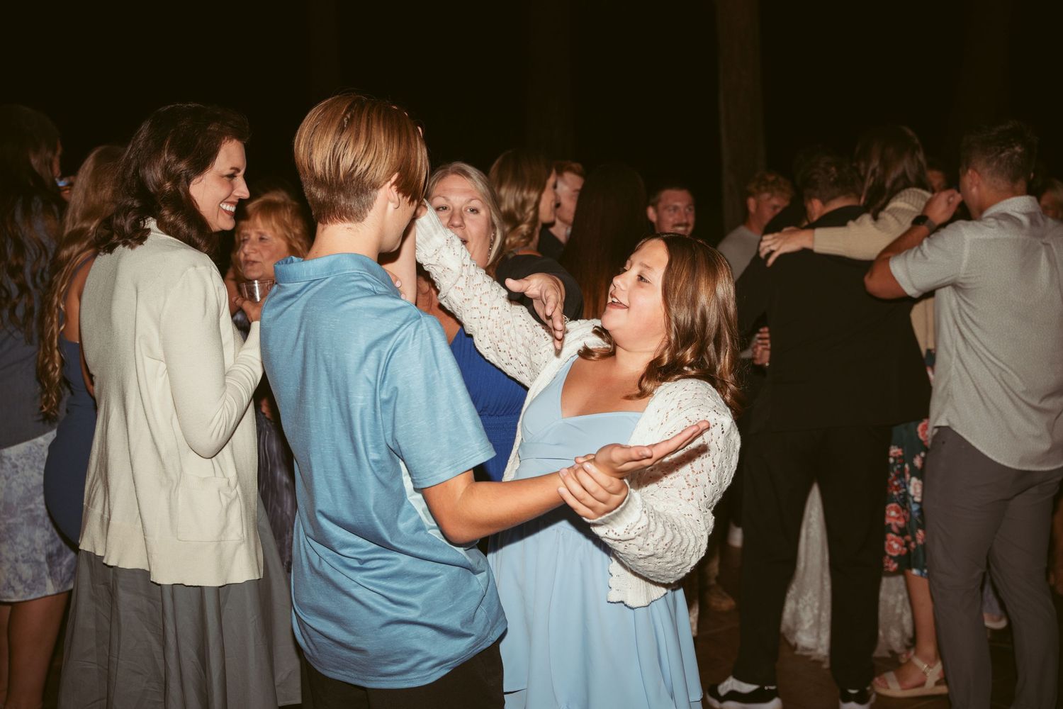 Guests laugh and dance together at a lively outdoor wedding celebration.