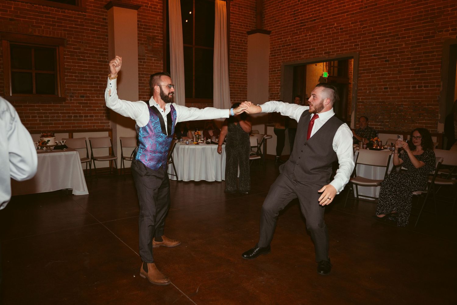 Wedding guests dancing energetically on a dimly lit dance floor with brick walls in the background.