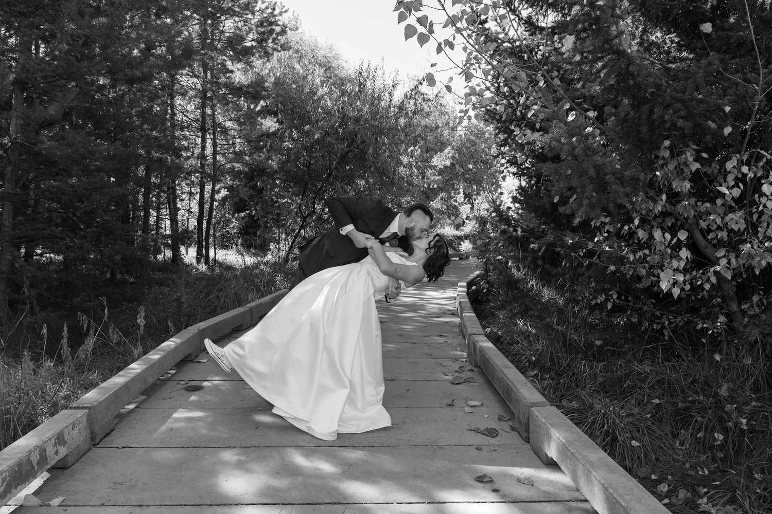 A dramatic black and white wedding photo of a couple dipping on a wooden boardwalk.
