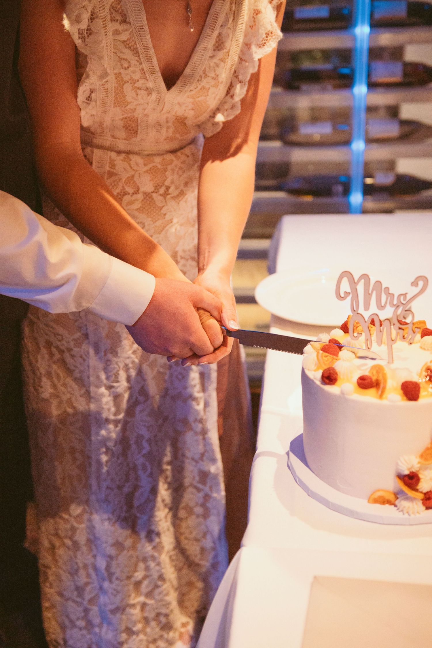Close-up of hands decorating a white wedding cake with small strawberries.