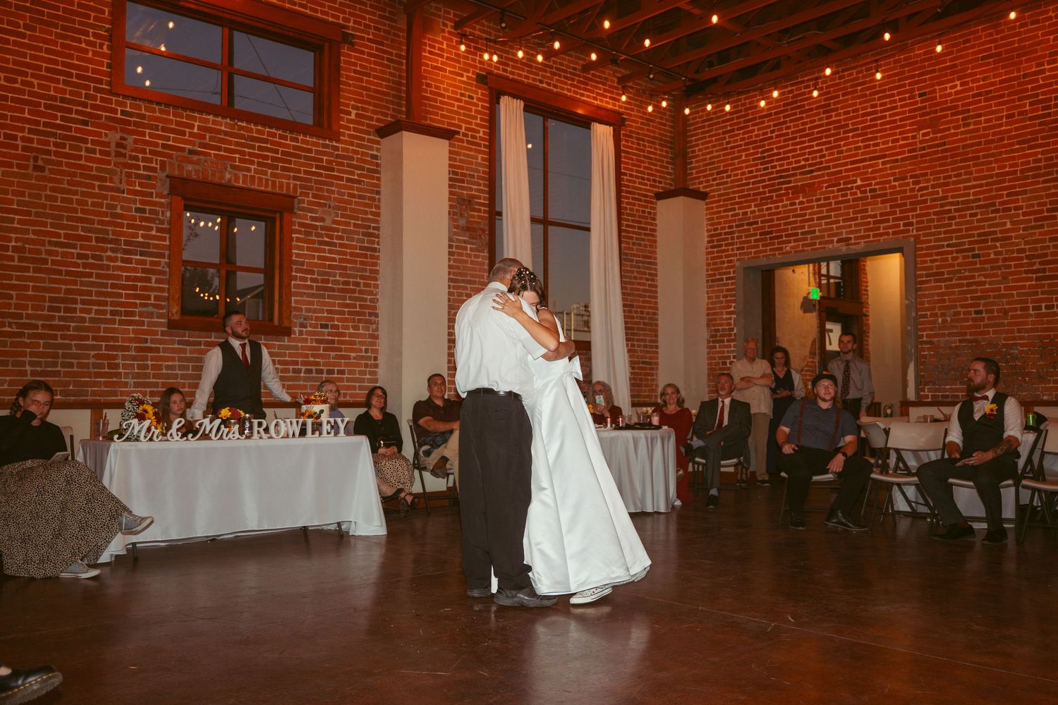 Wedding reception dance in a rustic brick building with warm lighting and hardwood floors.