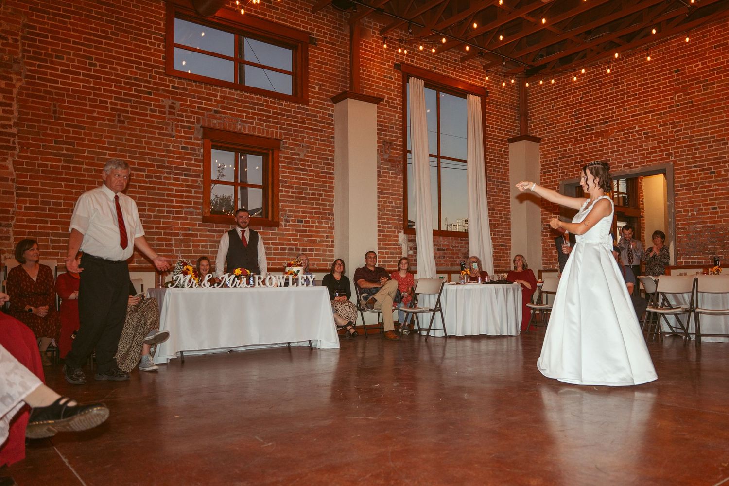 A wedding celebration in a rustic brick venue with string lights and white tablecloths.