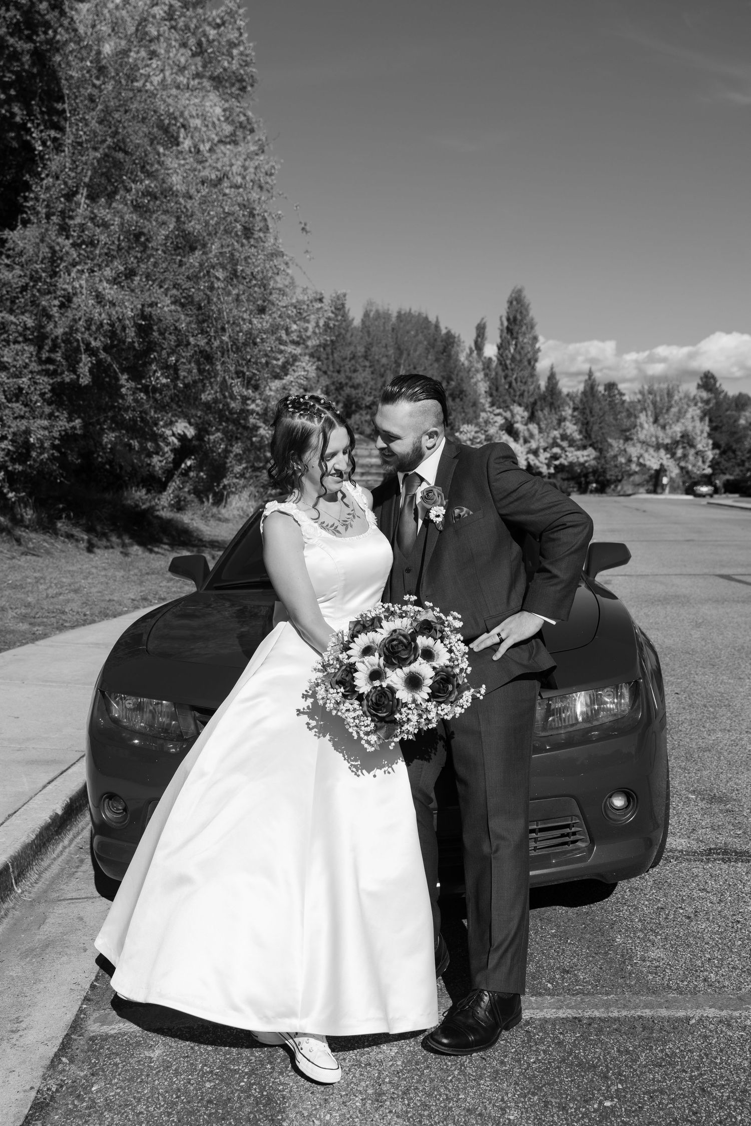 A black and white wedding portrait with a sunflower bouquet and car backdrop.