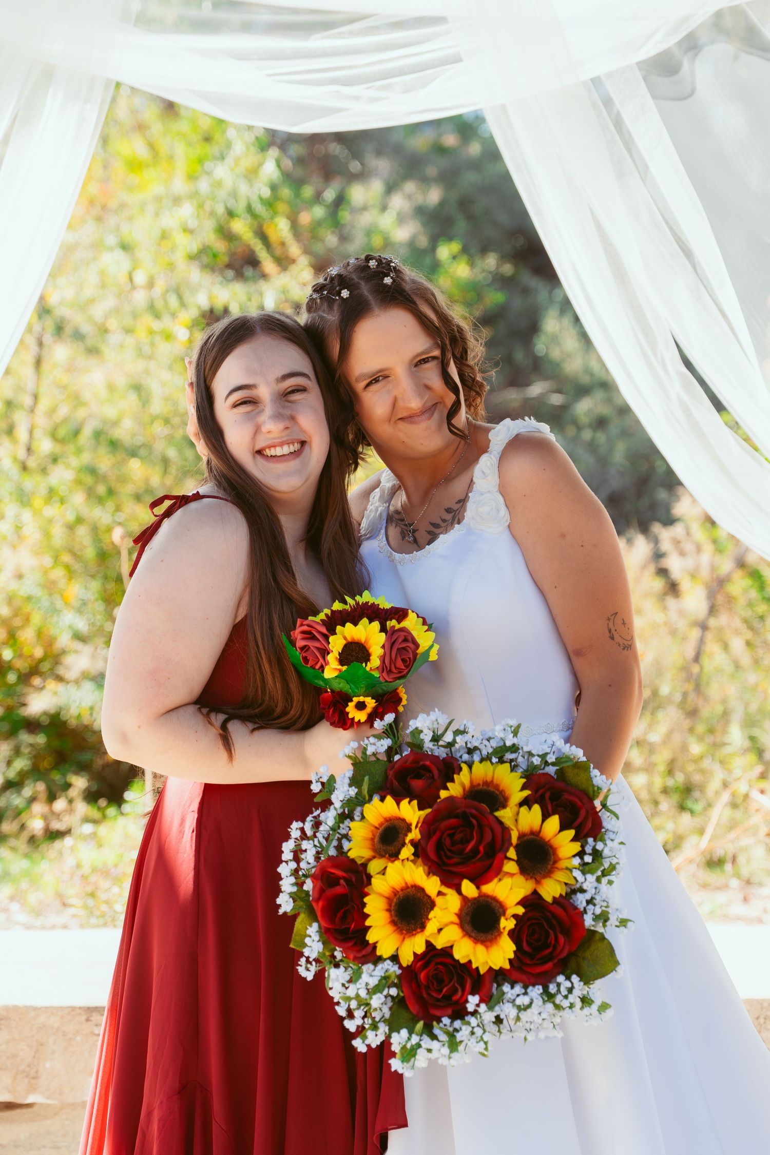 Wedding couple and attendant pose with bright sunflower bouquets under white draped outdoor pavilion.