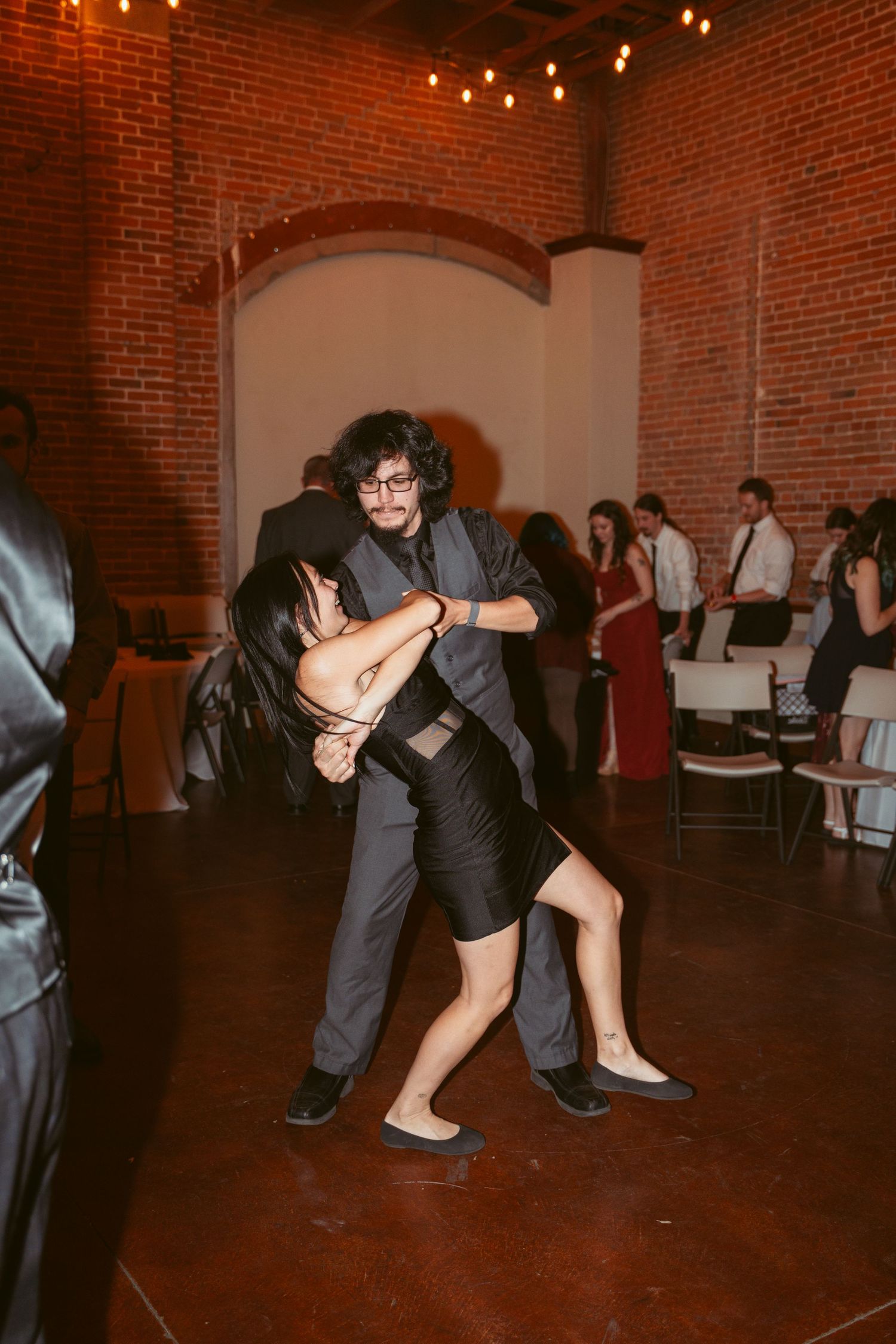 Couples executing swing dance moves in a vintage brick venue with ambient lighting.