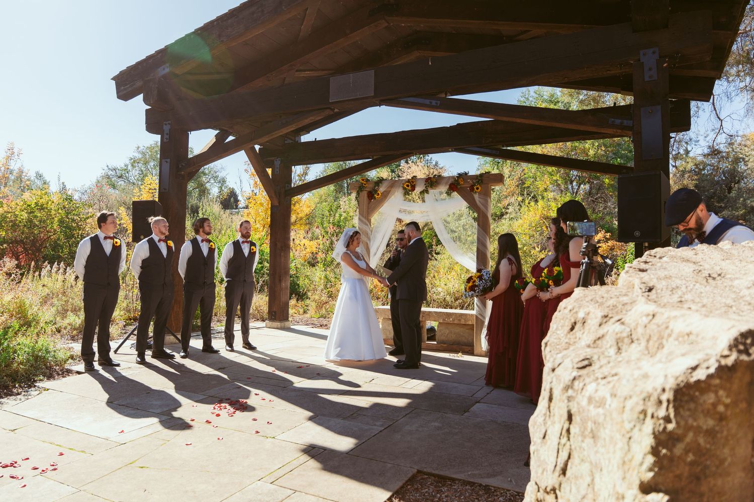 Panoramic shot of wedding ceremony setup with stone pillars and wooden beams.