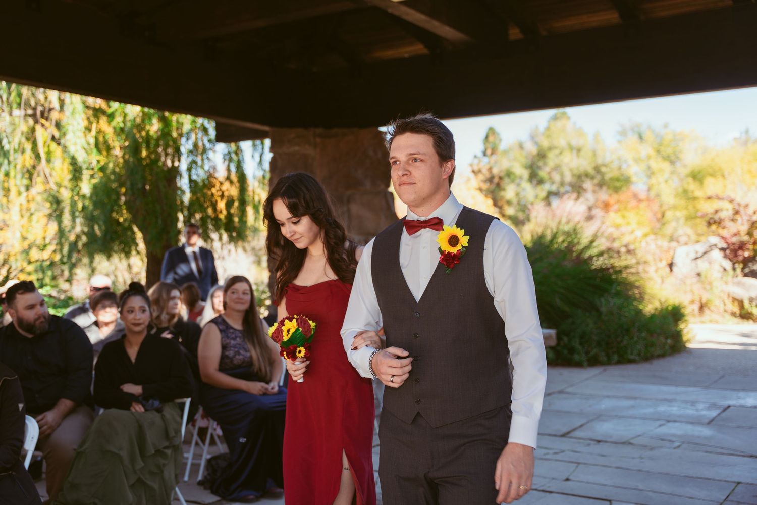 Wedding guests socialize during an outdoor reception under wooden pergola.