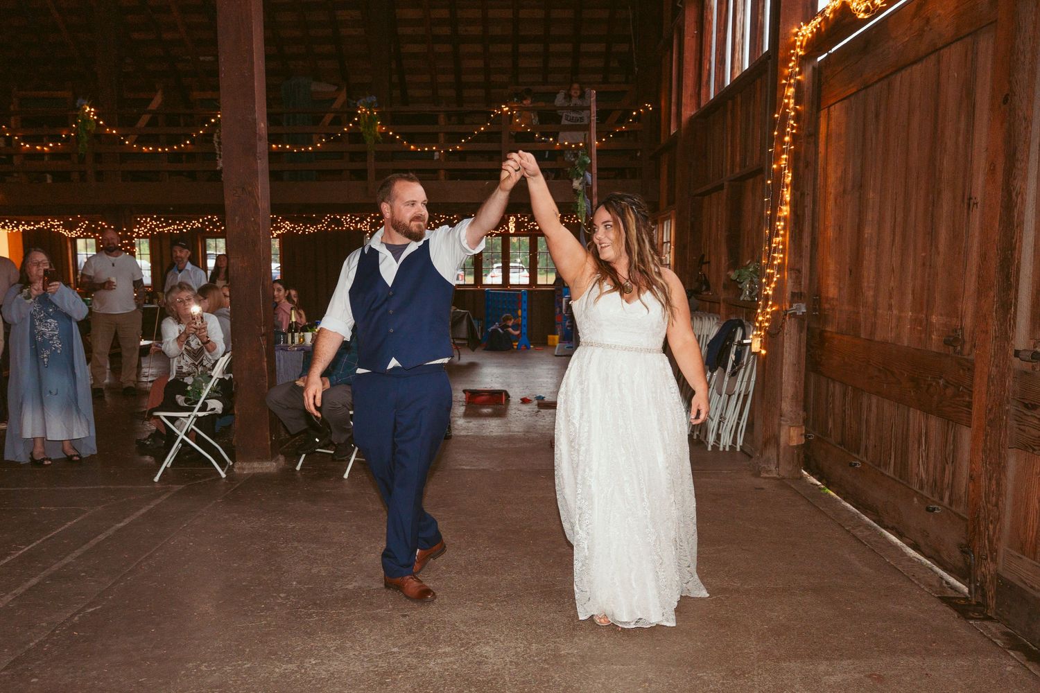 Couple dances in a beautifully lit rustic barn during their wedding reception.