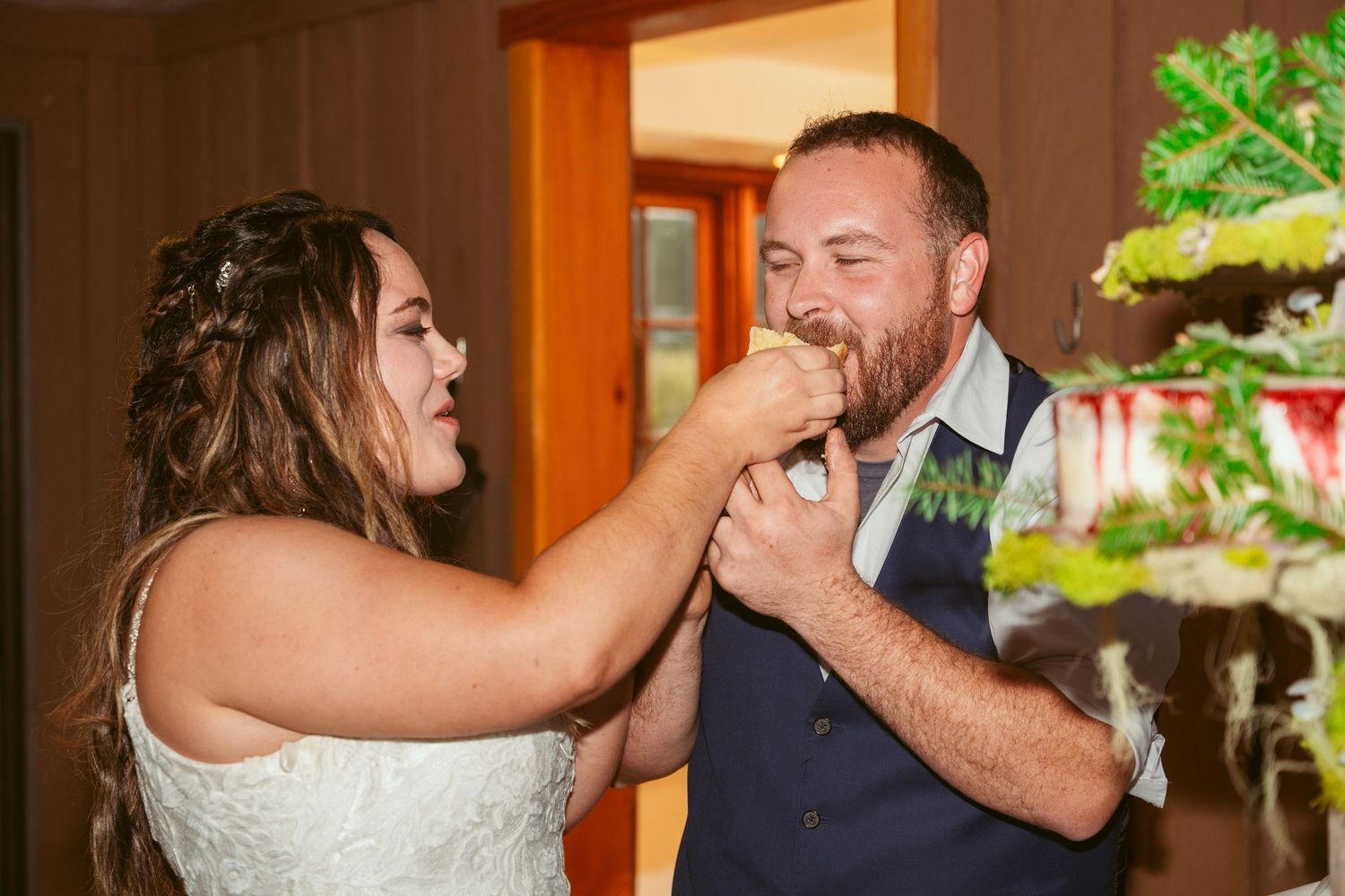 Newlyweds playfully feed each other wedding cake during their reception celebration.