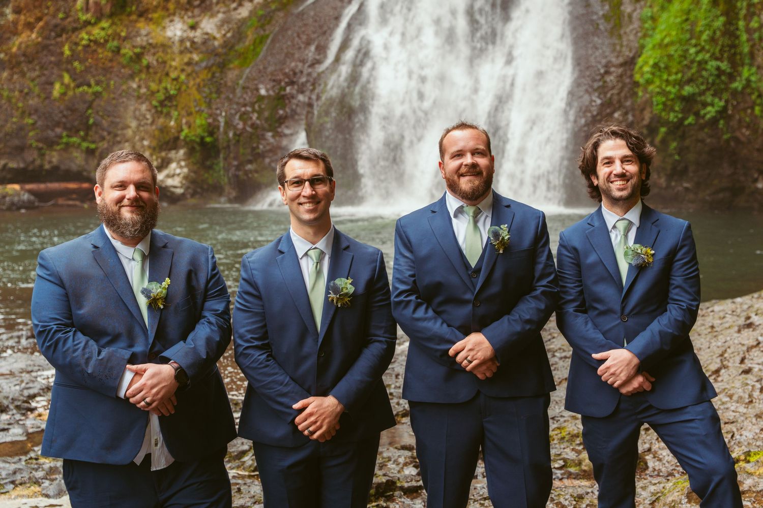 Groomsmen line up in matching navy suits against a waterfall backdrop.