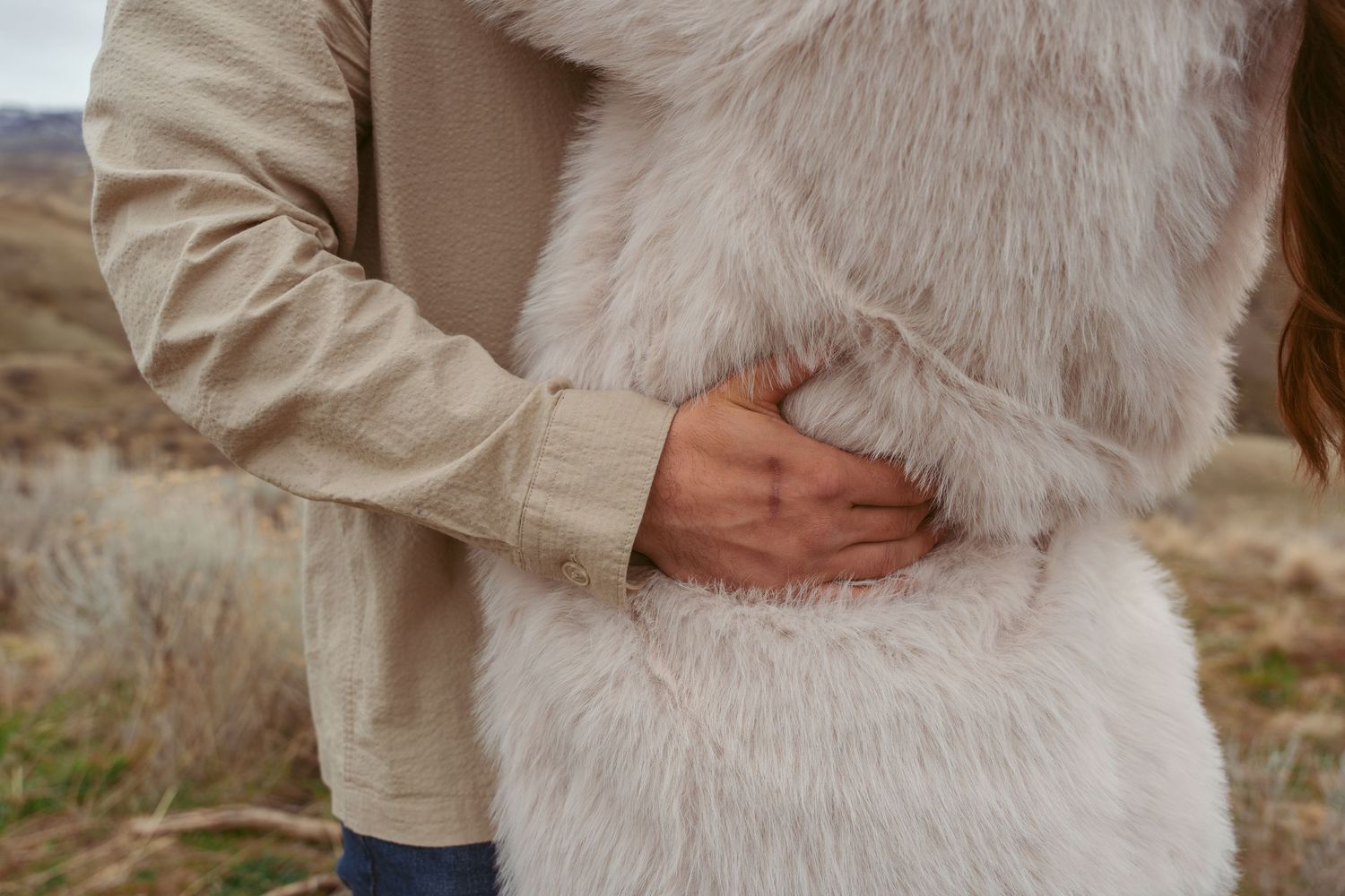 Close-up of hands embracing against a fluffy white fur coat outdoors.