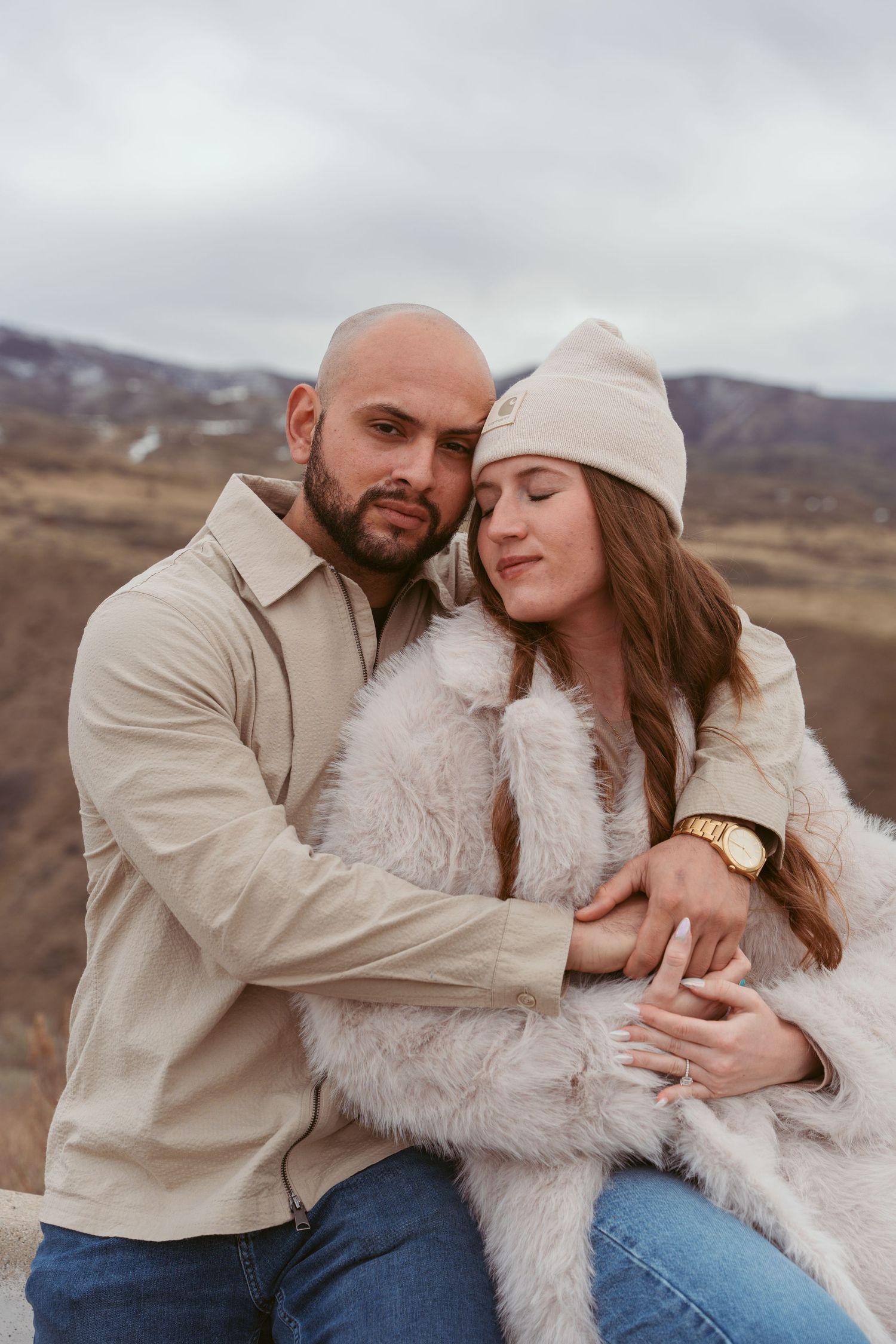 A couple in casual winter attire shares a tender moment against a mountainous landscape.