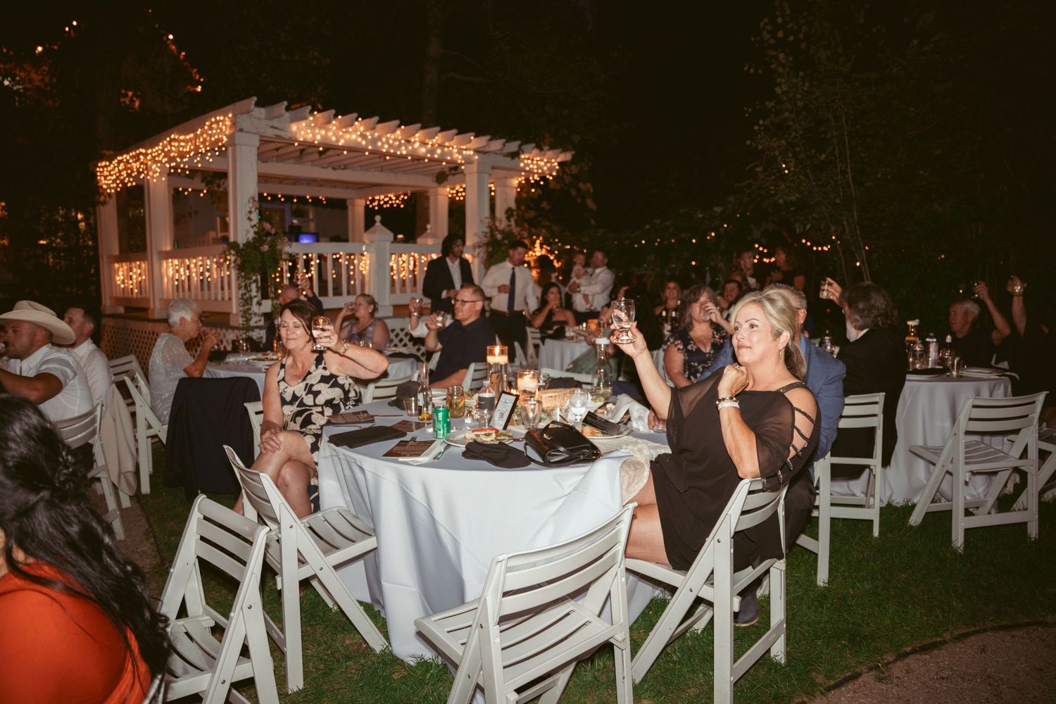Wedding reception guests seated at decorated tables under string lights in an outdoor garden setting.